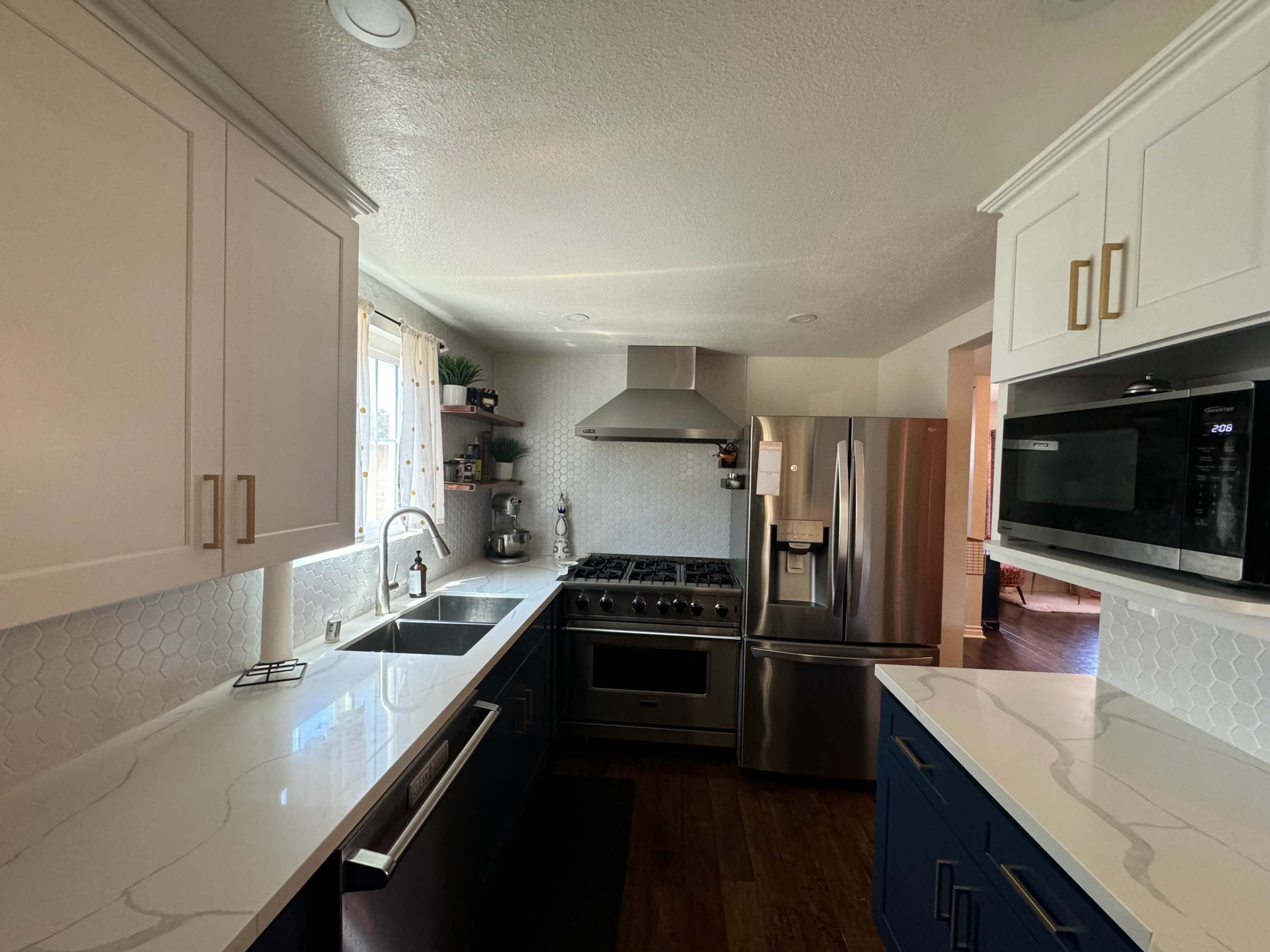 The image shows a modern kitchen featuring white upper cabinets, blue lower cabinets, stainless steel appliances, and a large island with a sink.