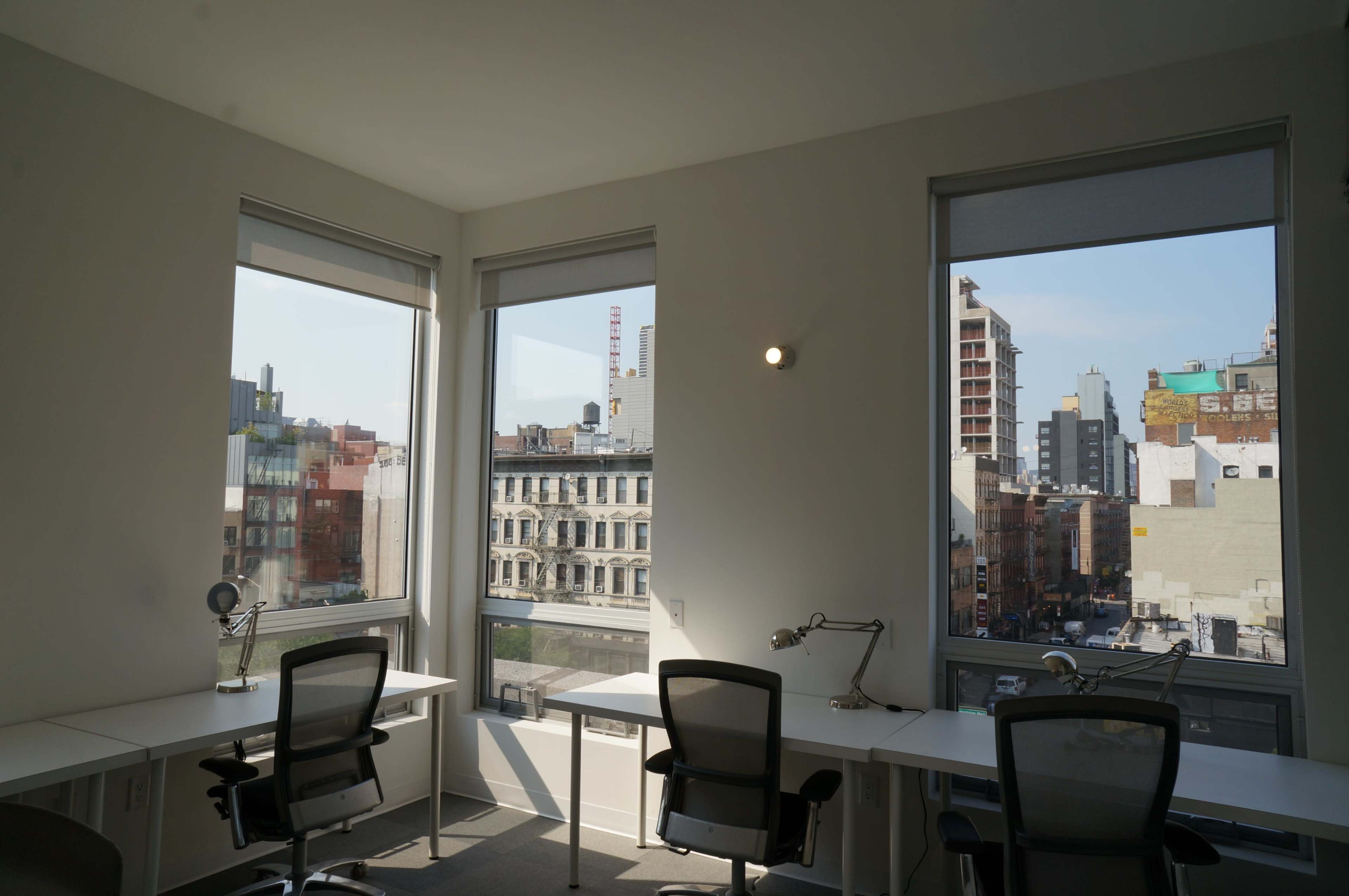 A bright office space with two empty desks and large windows overlooking a cityscape.