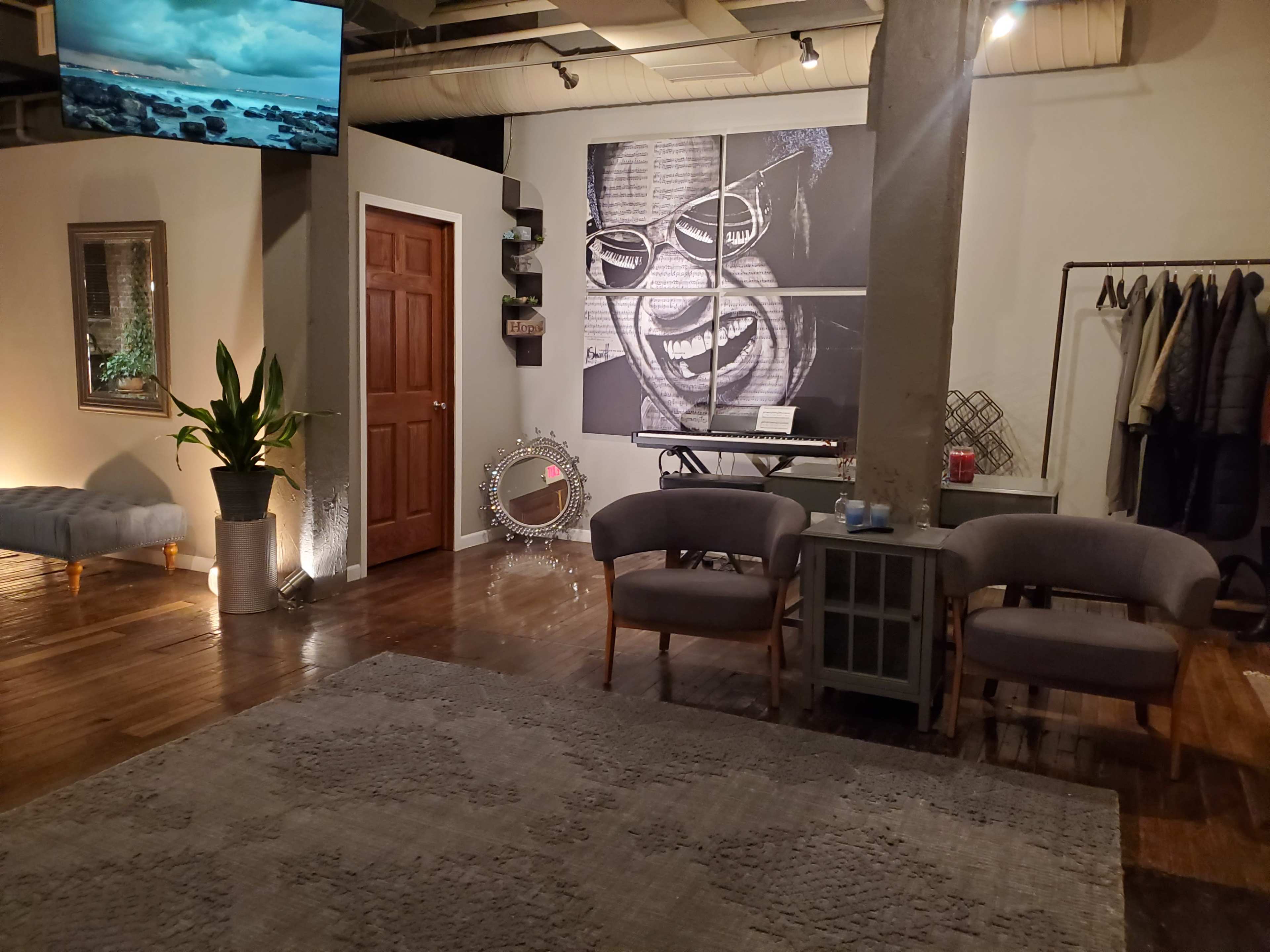 A warmly lit interior space featuring a seating area with two chairs, a large wall art piece of a smiling face, and a doorway leading to another room.