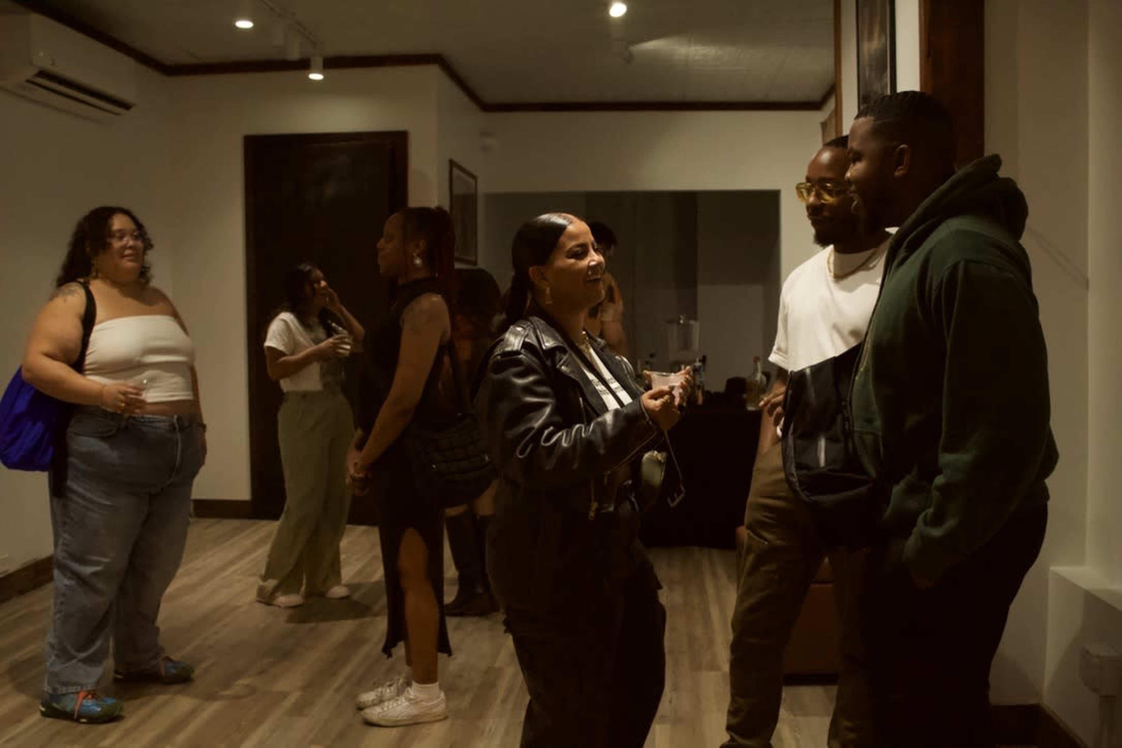 A group of people converse in an indoor space with wooden flooring and art on the walls.