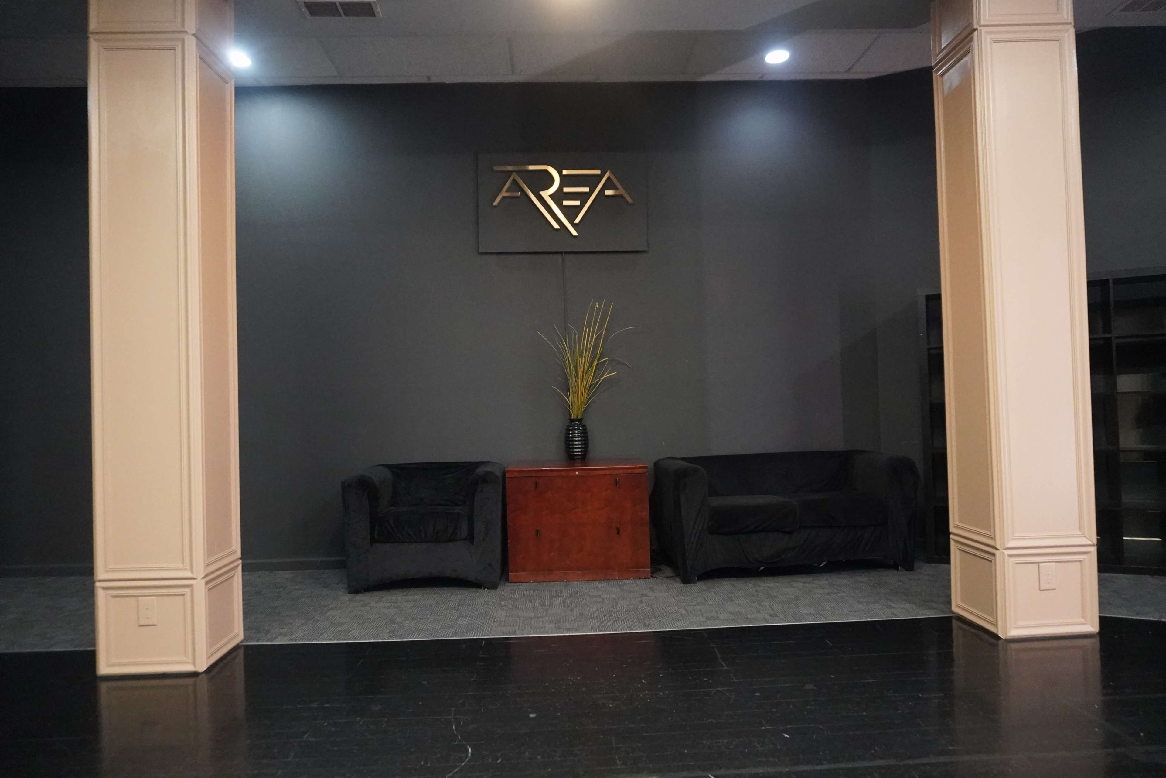 A modern interior space featuring two black couches, a wooden table, and decorative plants against a dark wall with the word "AREA" displayed above.