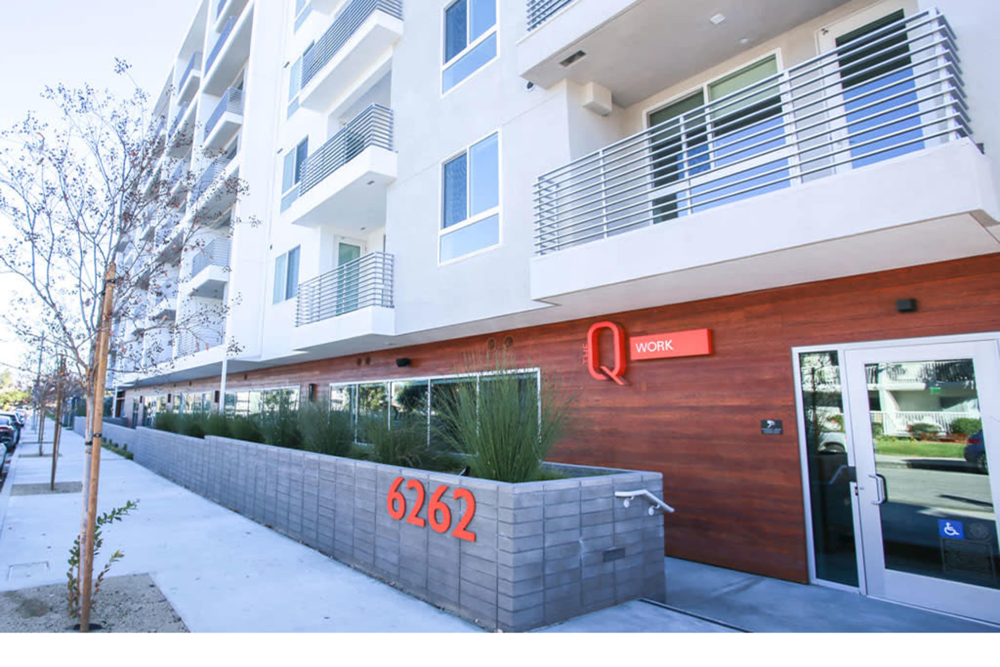 A modern multi-story building with a wooden accent wall, large windows, and a prominent address number "6262" displayed in red at the entrance.