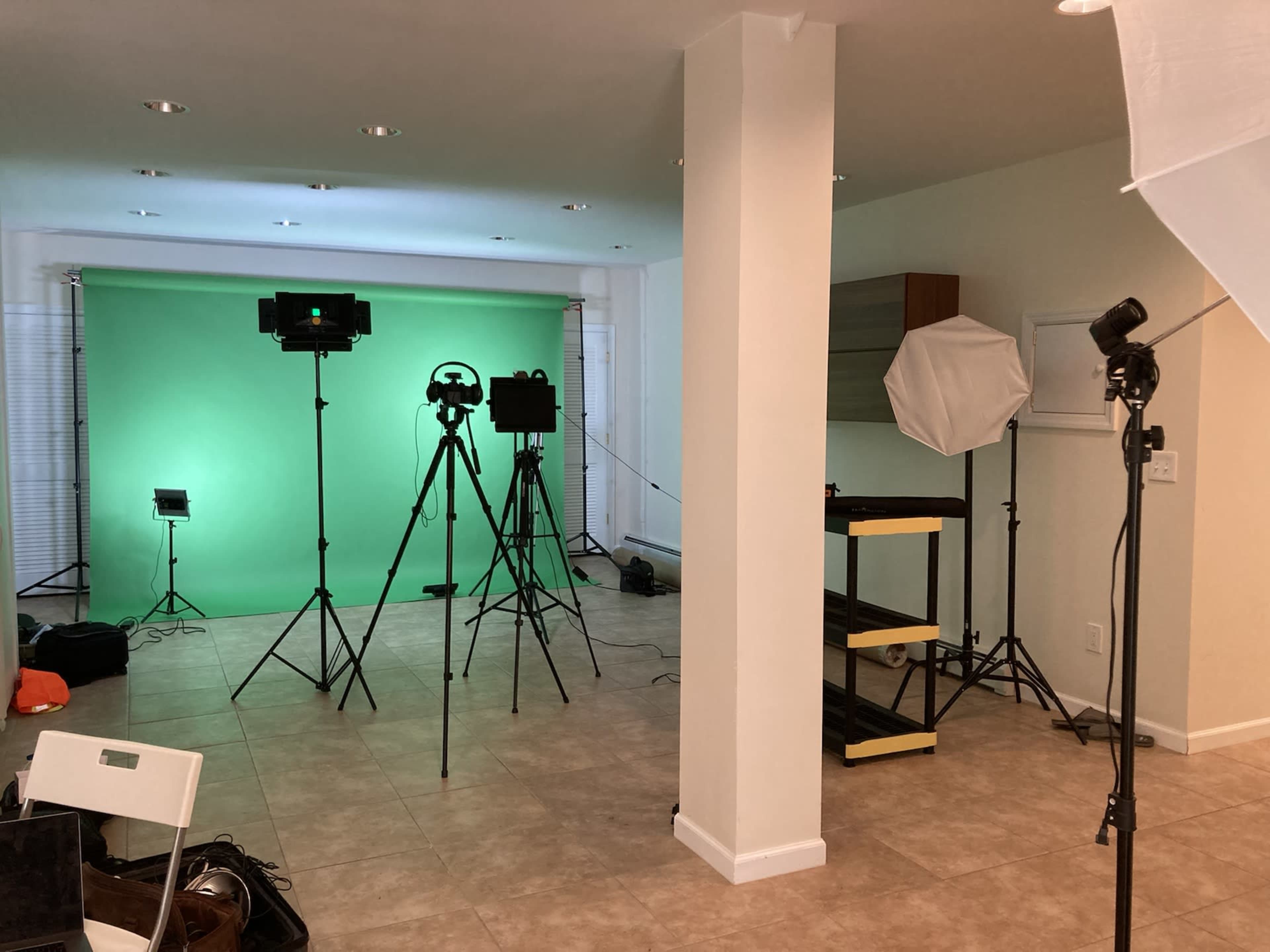 A studio setup featuring green screens, lighting equipment, and tripods arranged in a room with tiled flooring.