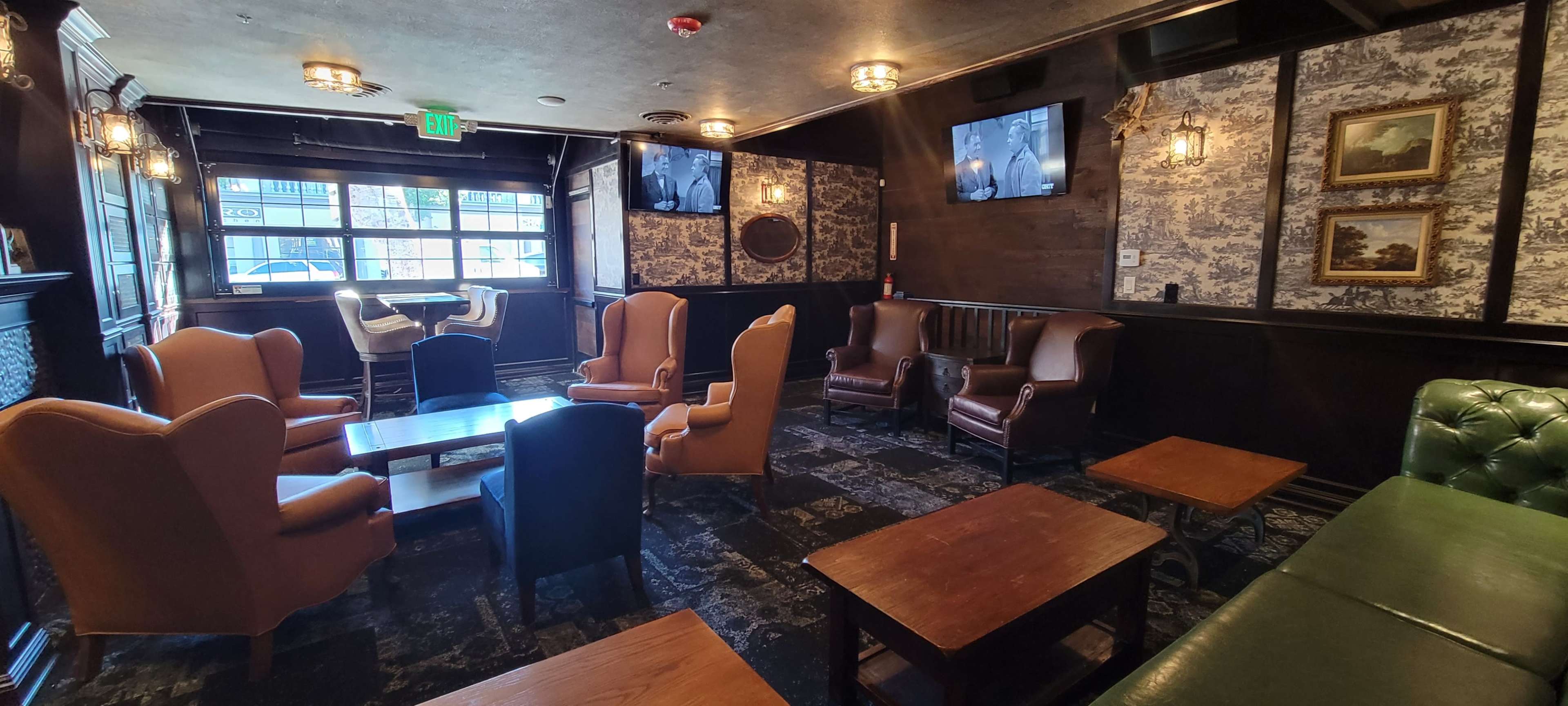A cozy lounge area with various seating arrangements, including leather chairs and wooden tables, and large windows letting in natural light.