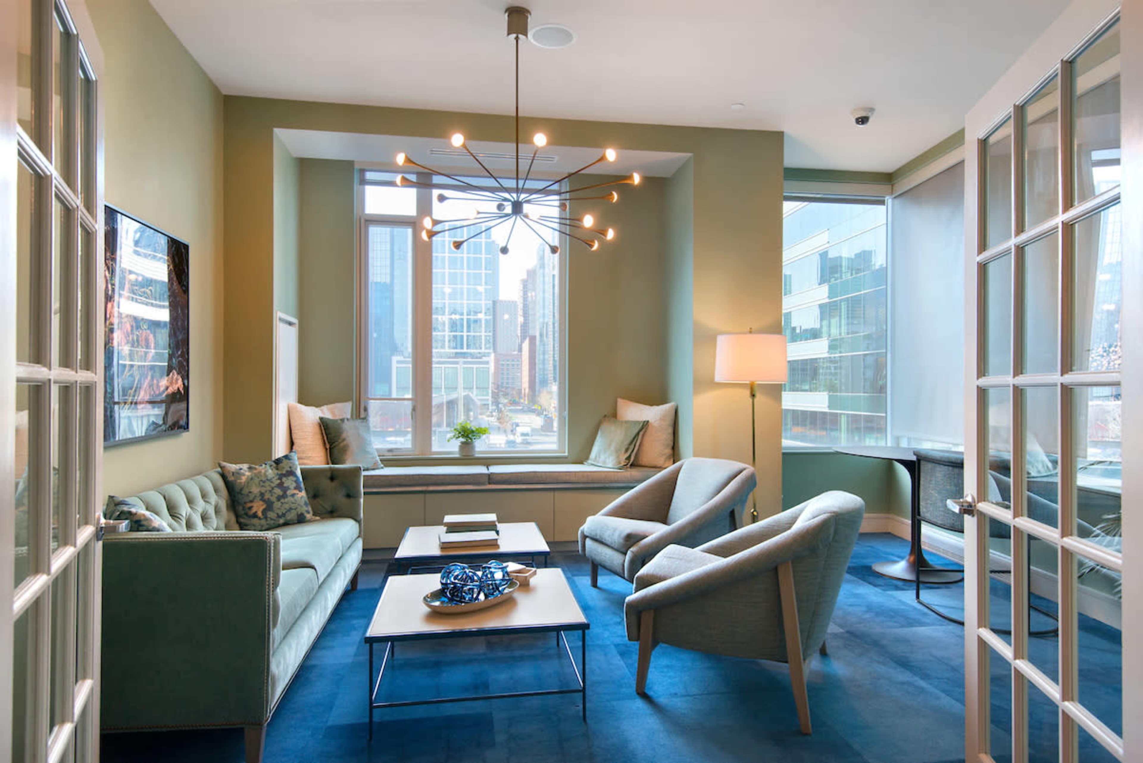 A modern lounge area with green walls, contemporary furniture, and large windows overlooking a cityscape.