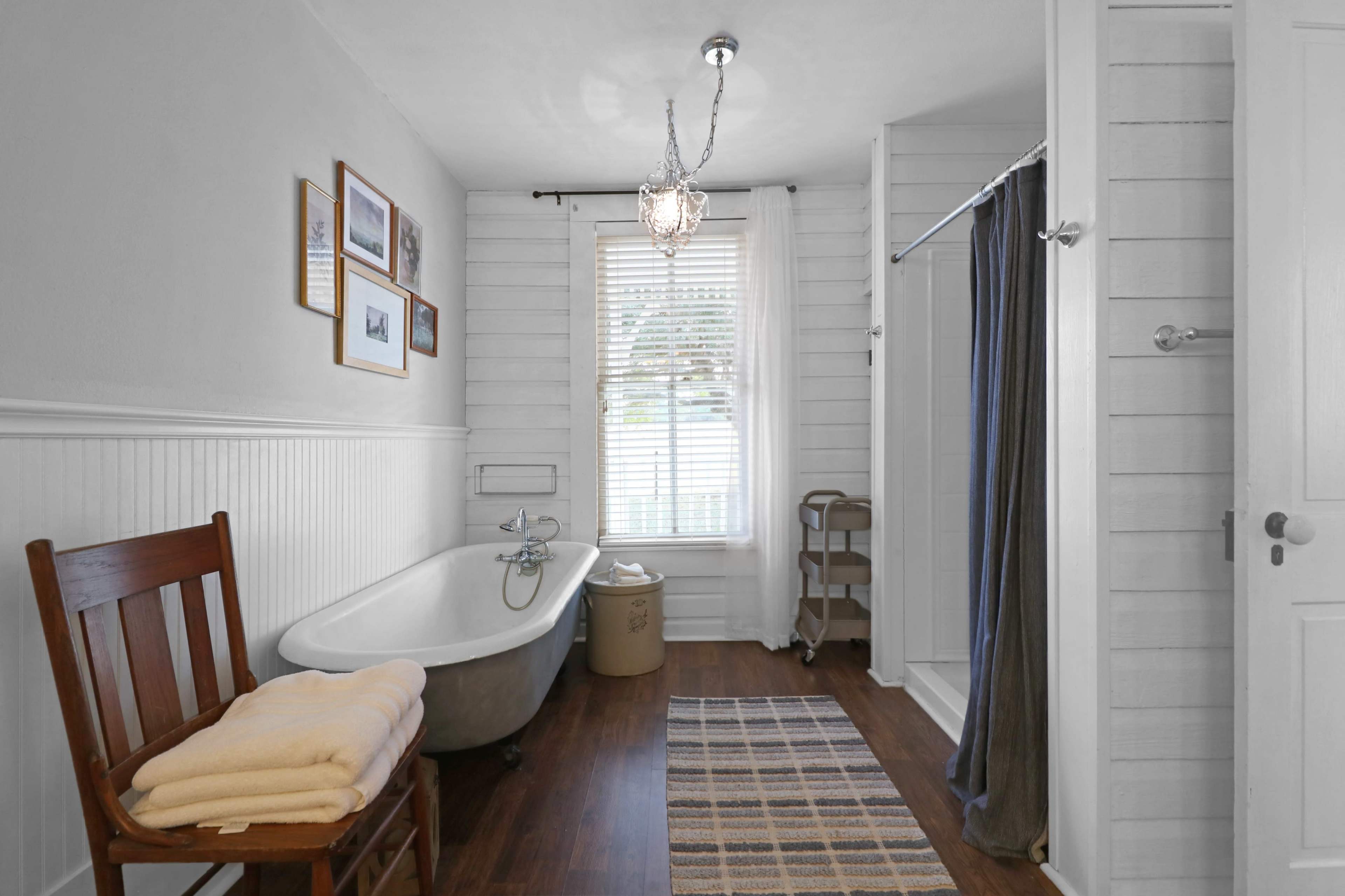 A bathroom featuring a freestanding bathtub, a shower area, a wooden chair with towels, and framed pictures on the walls.