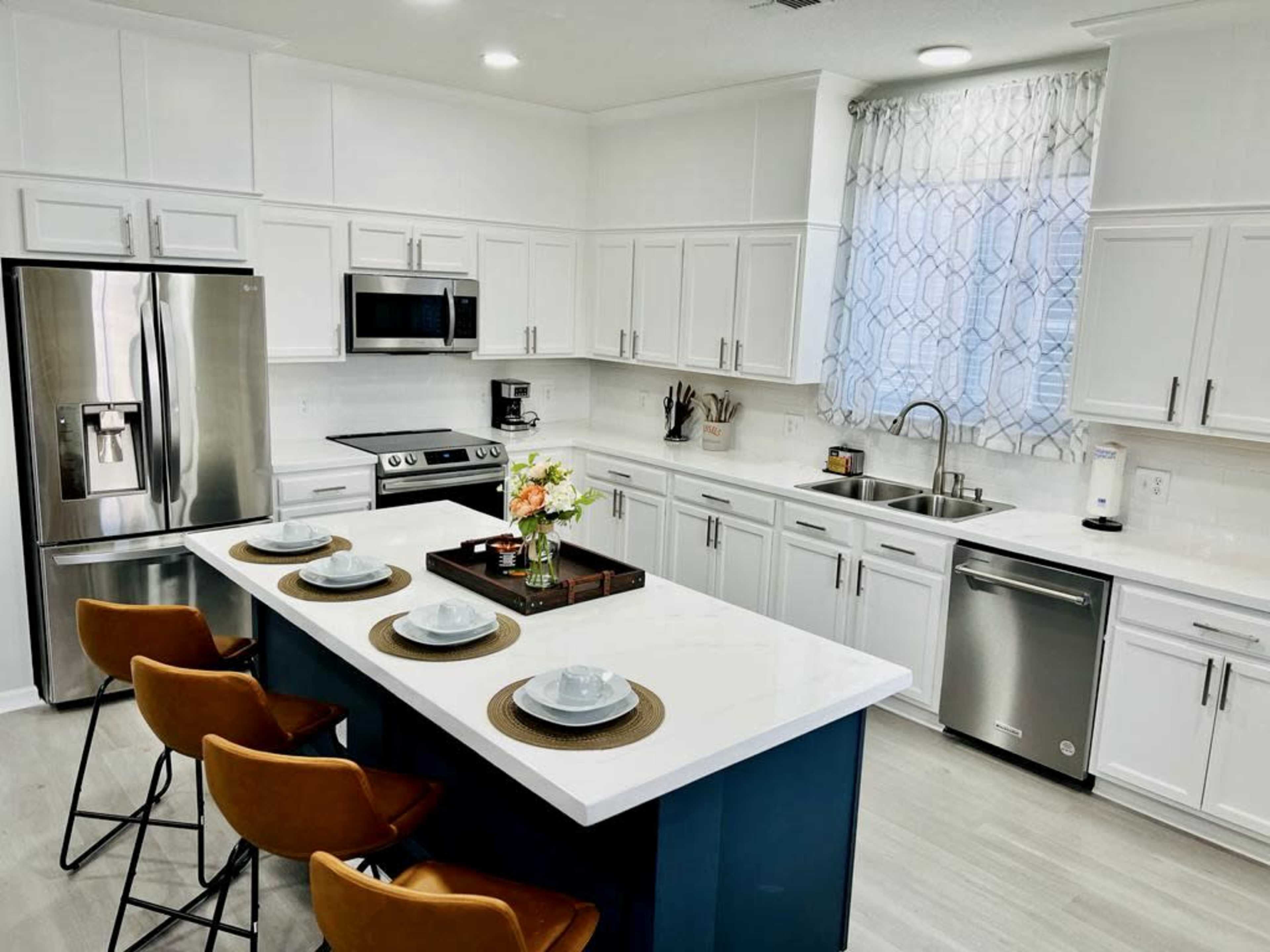 A modern kitchen features white cabinetry, stainless steel appliances, and a central island with seating for four.