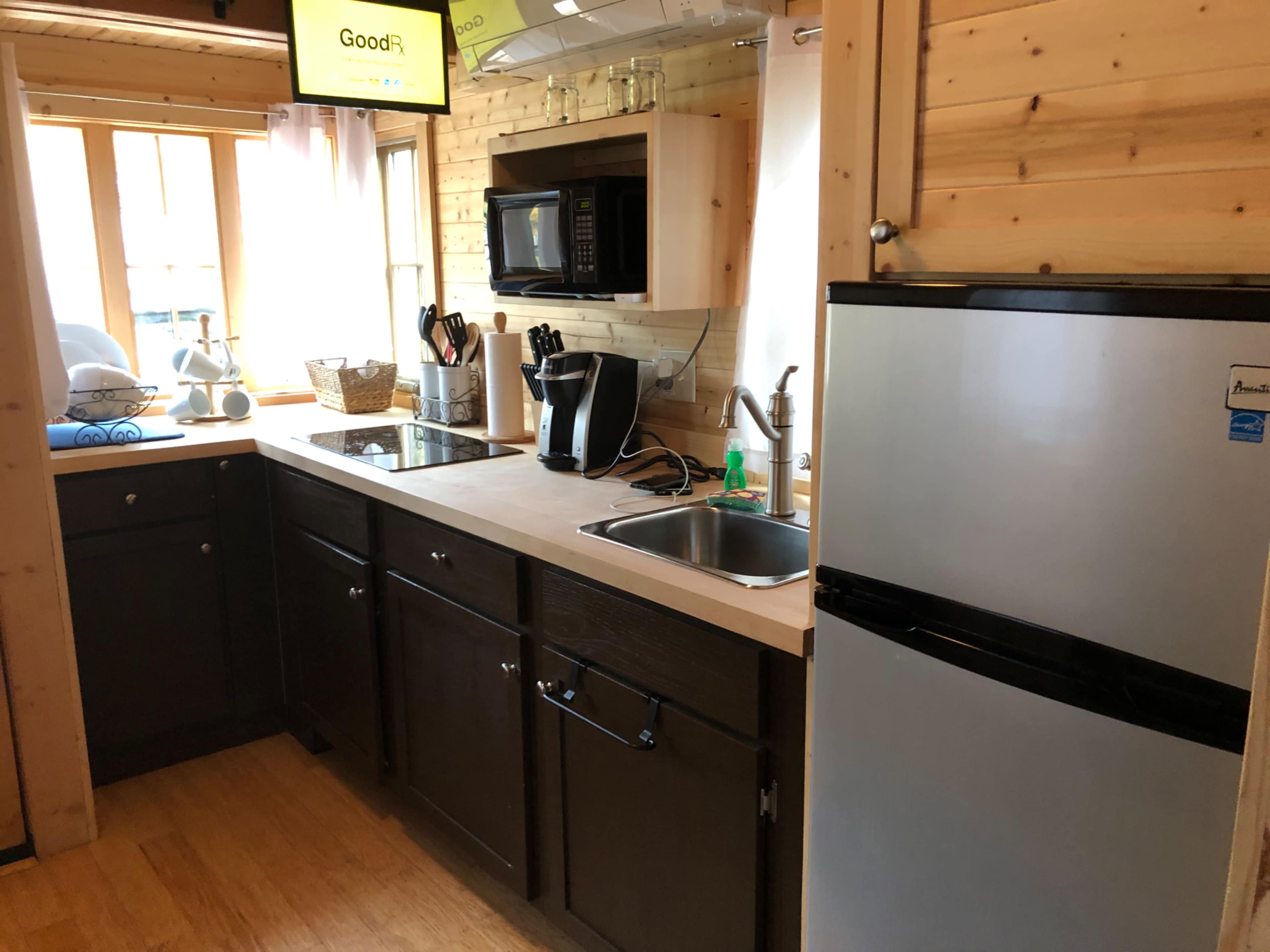 A small kitchen featuring a microwave, sink, and refrigerator, with wood paneling and natural light coming through a window.