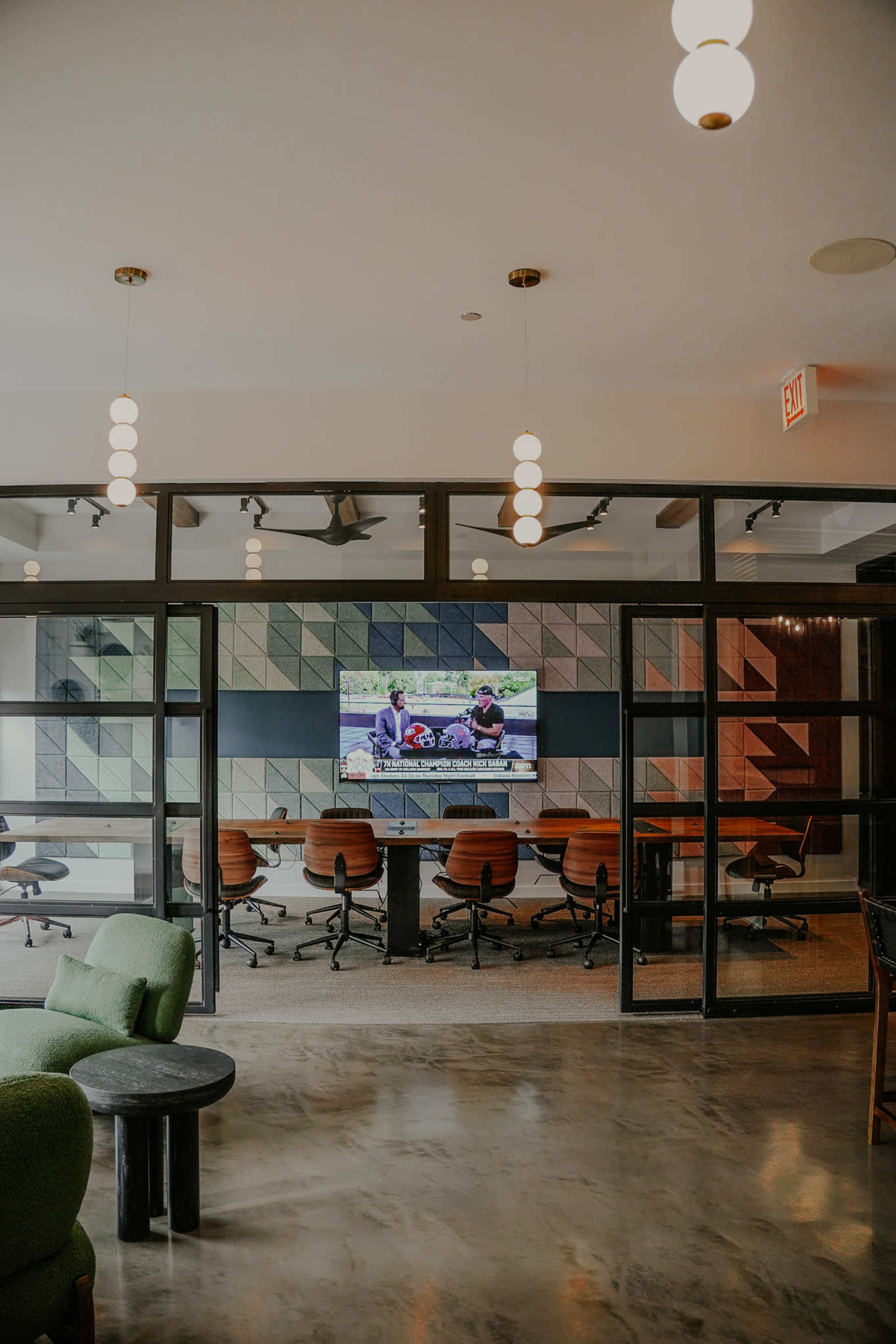 The image shows a modern office space featuring a conference room with a large screen and stylish seating areas visible through glass walls.