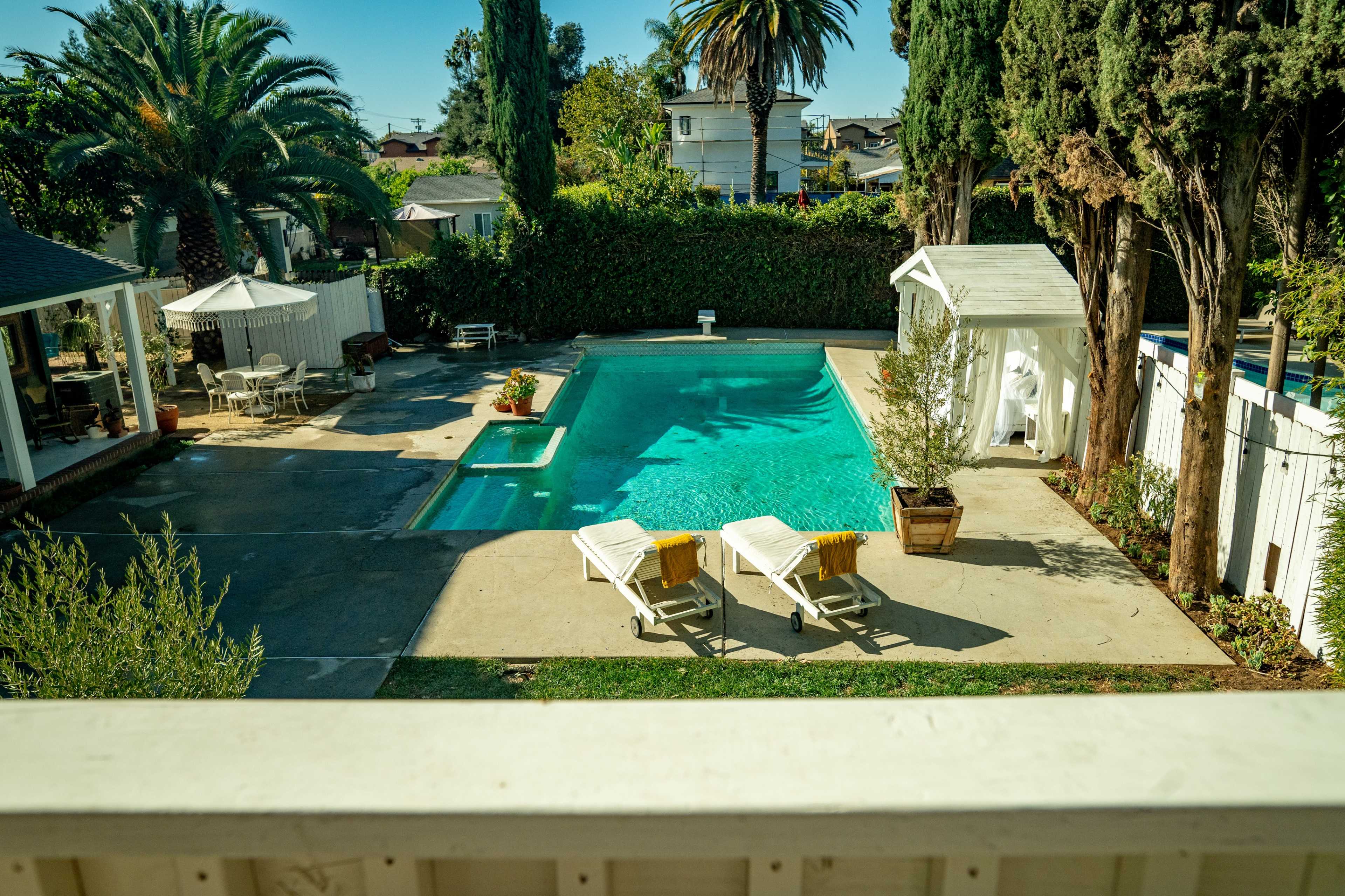 The image shows a backyard pool area with two lounge chairs beside a turquoise pool, surrounded by palm trees and greenery.