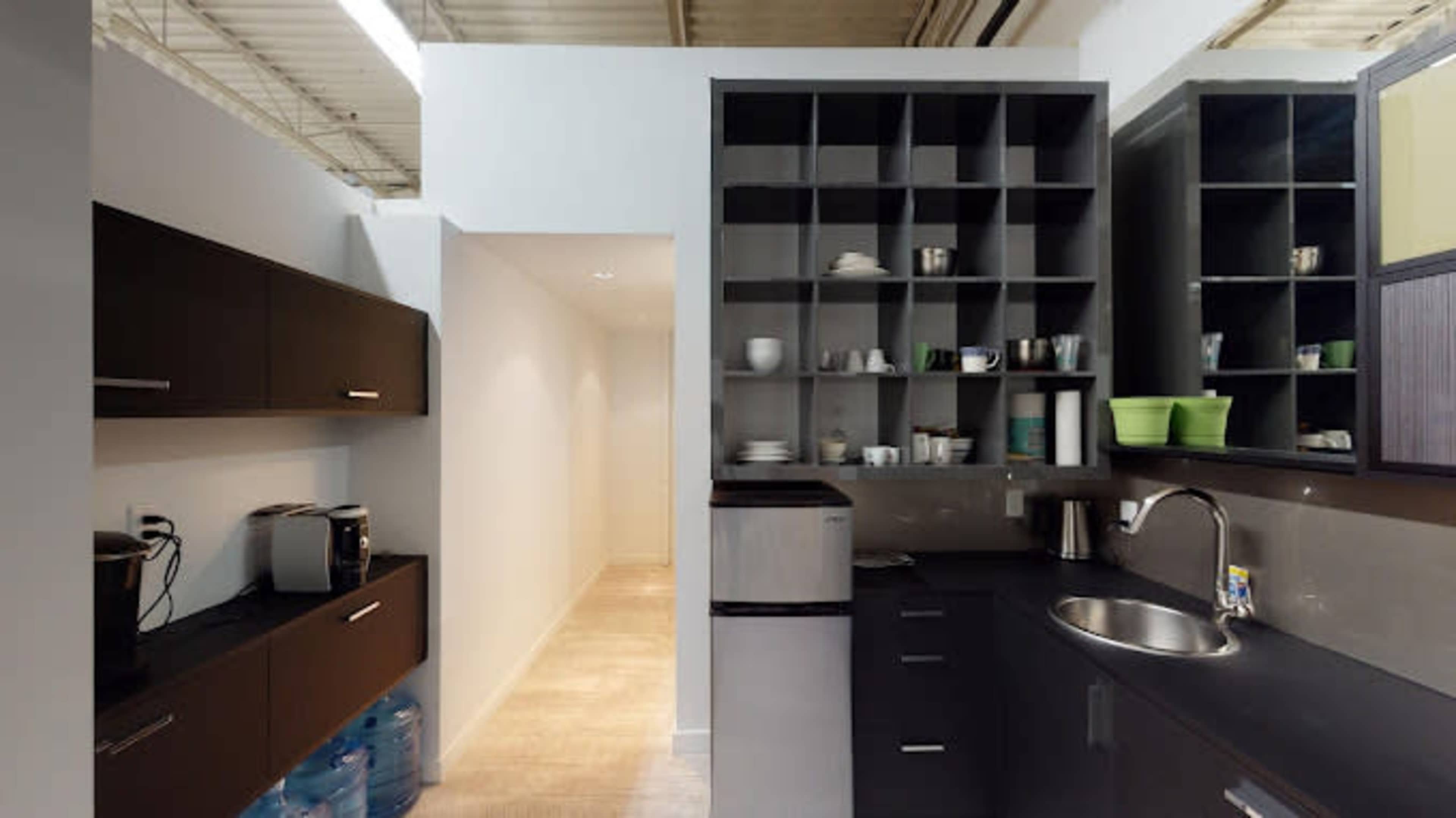 A modern kitchen layout with dark cabinets, a sink, a compact refrigerator, and shelves displaying cups and utensils, alongside a narrow hallway.