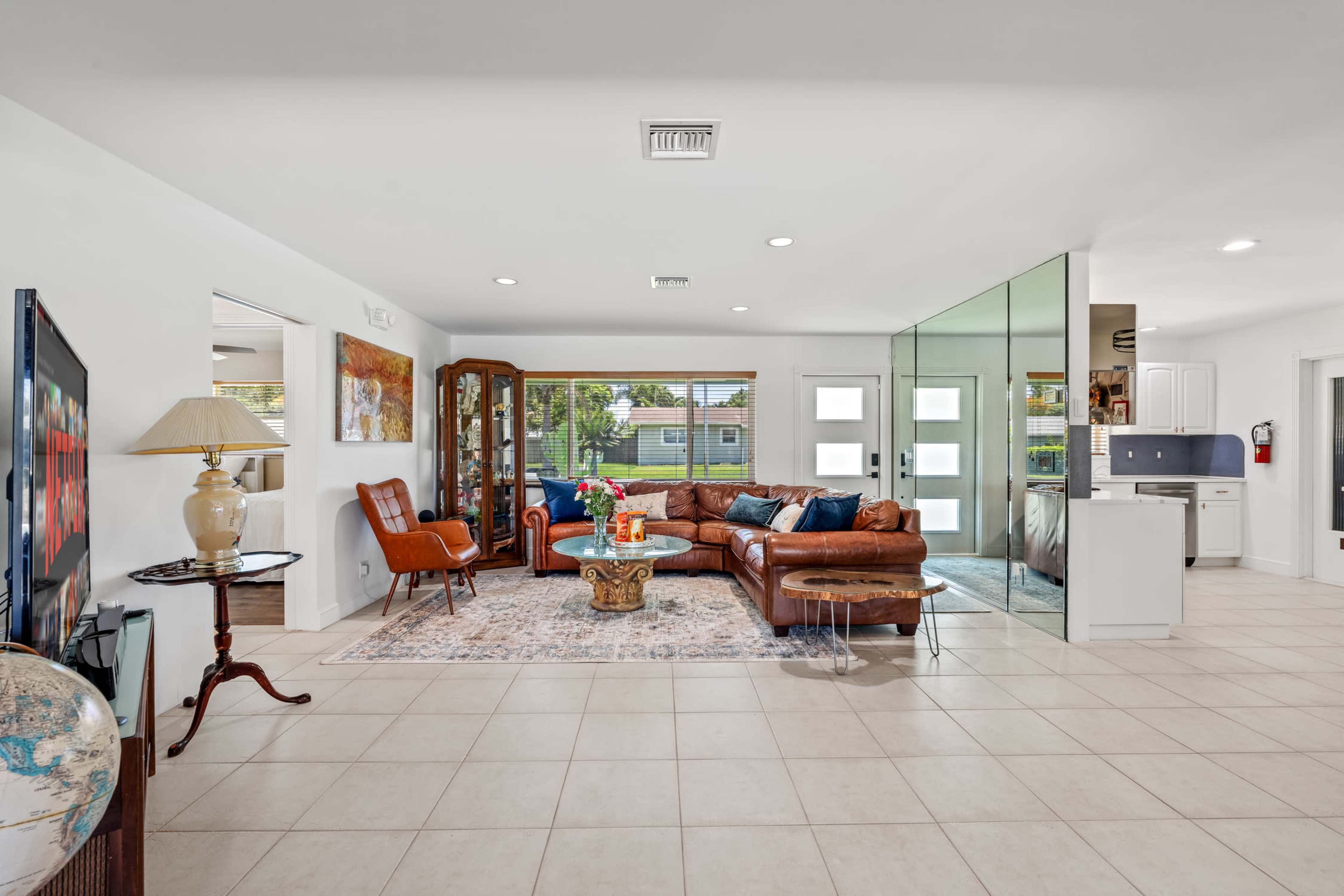 The image shows a modern living room with a leather sofa, glass-paneled walls, and tiled flooring, featuring a coffee table and decorative items.
