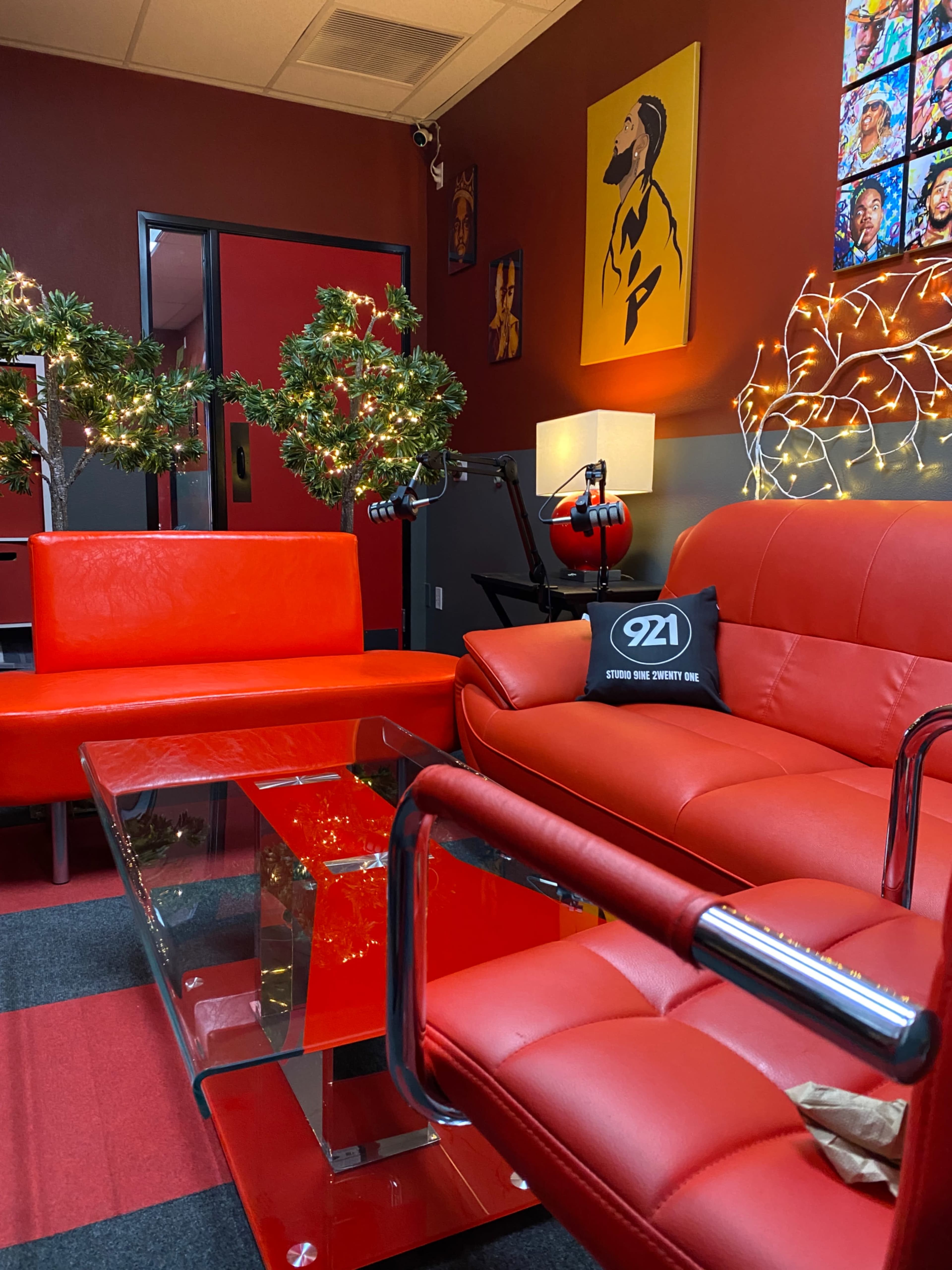 The image shows a modern lounge area with red furniture, a glass coffee table, and festive decorations, including wreaths and string lights.