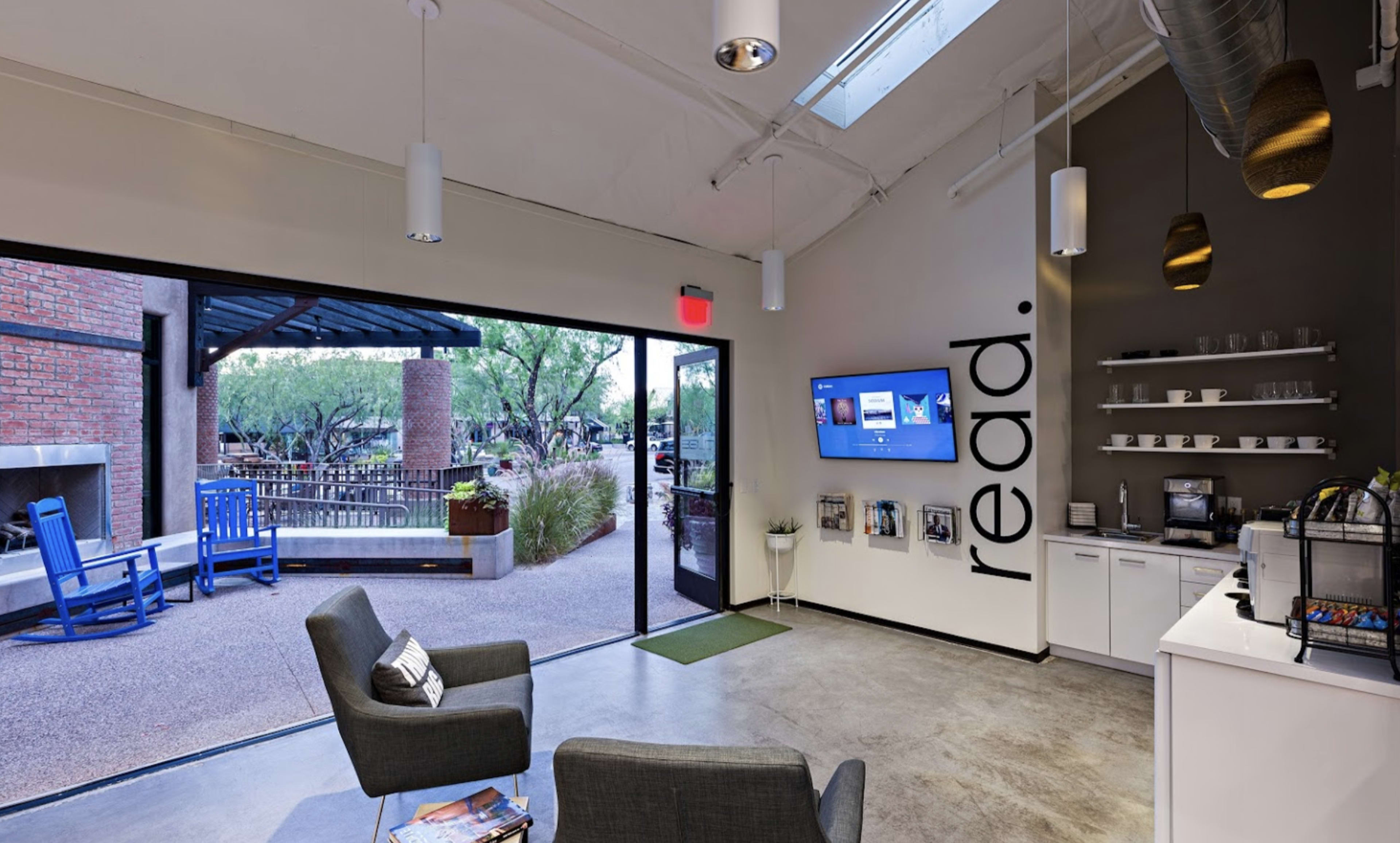 The image shows a modern indoor space with gray furniture, a large open door leading to an outdoor area, and a wall displaying the word "read."