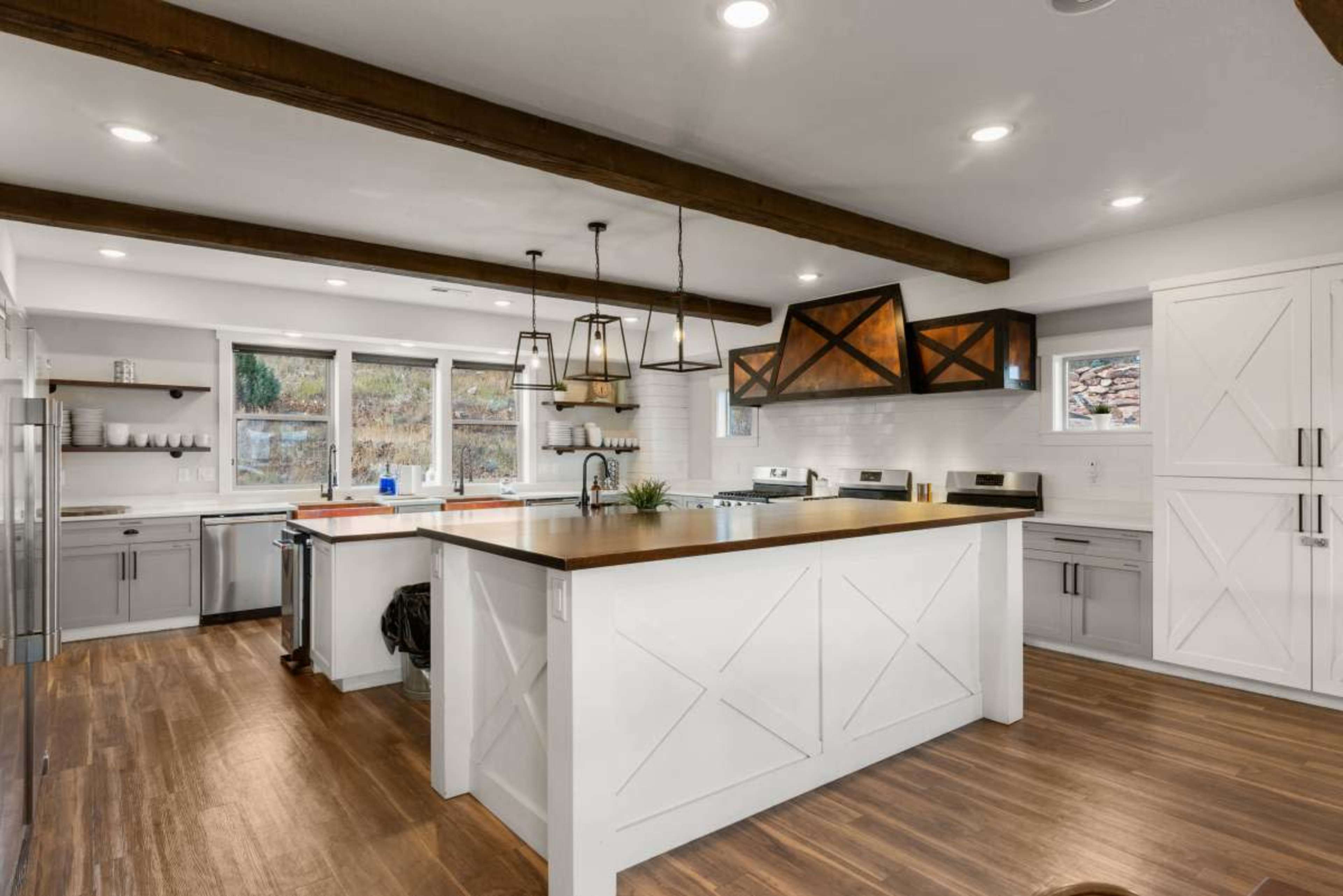 The kitchen features a central island with a wooden countertop, white cabinetry, and exposed wooden beams overhead.