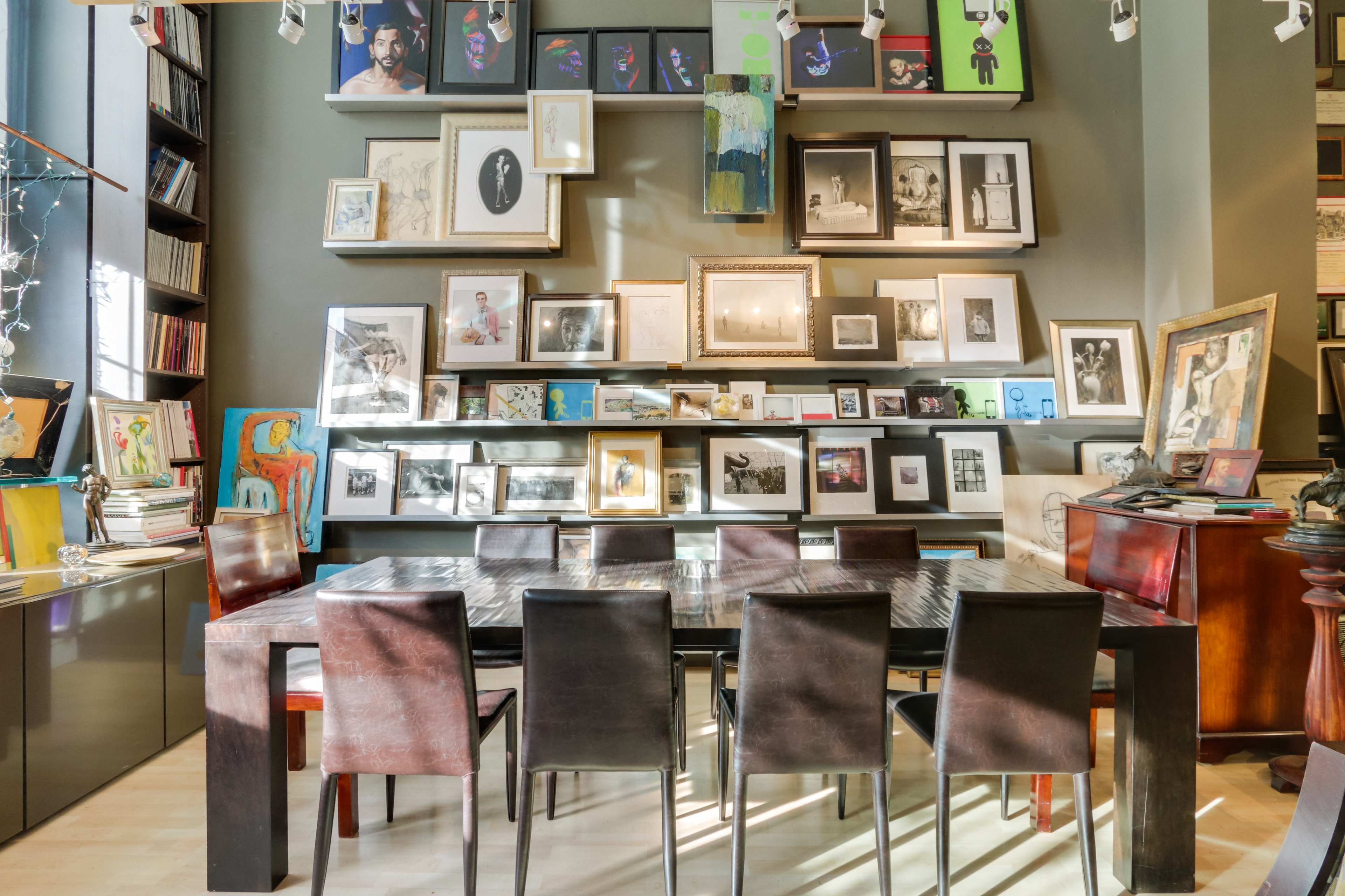 A large wooden table is surrounded by black chairs in a room filled with shelves of framed photographs and artwork.