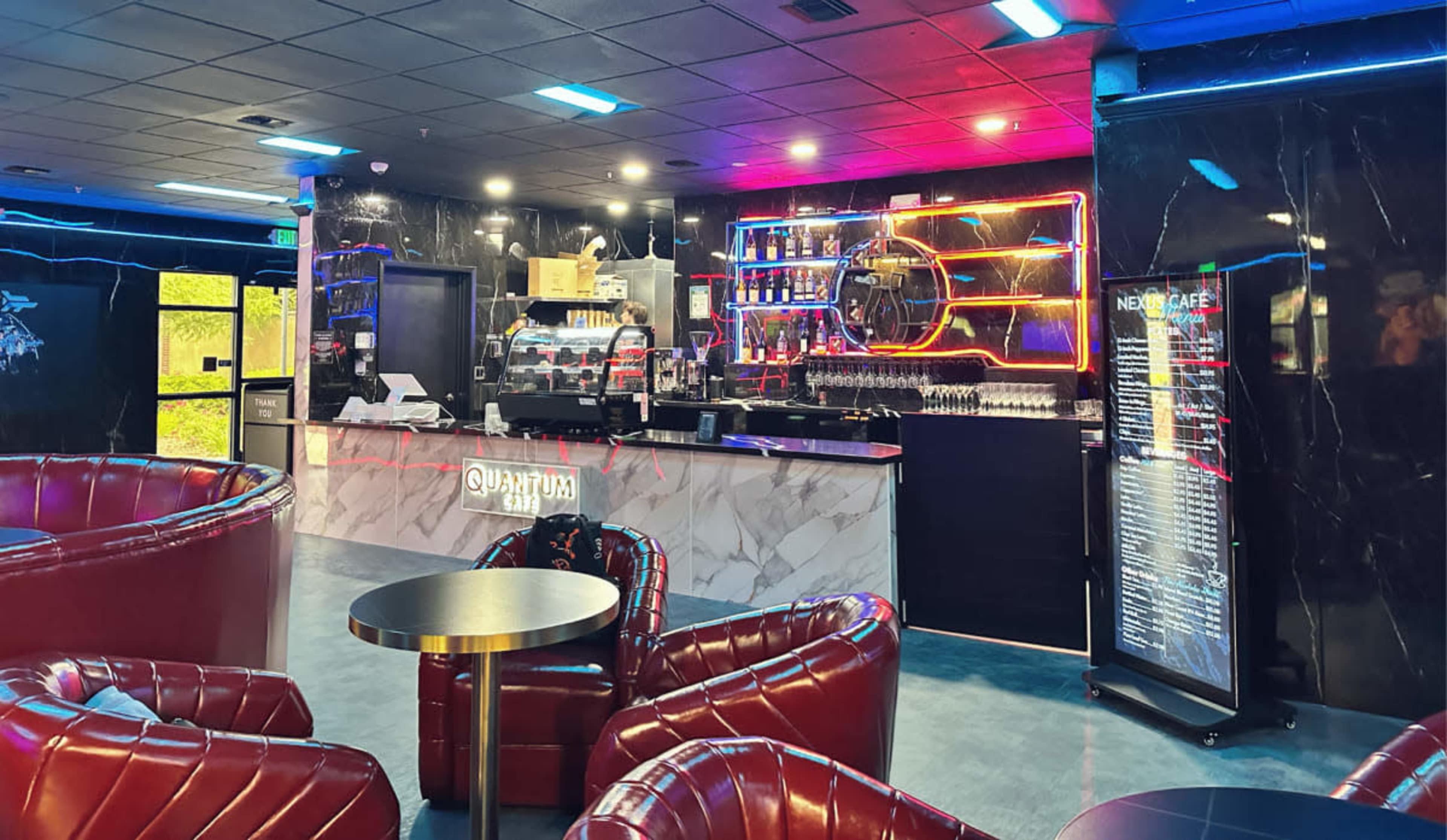 The image shows a modern cafe bar featuring a marble counter, brightly lit shelves of drinks, and stylish red leather seating.