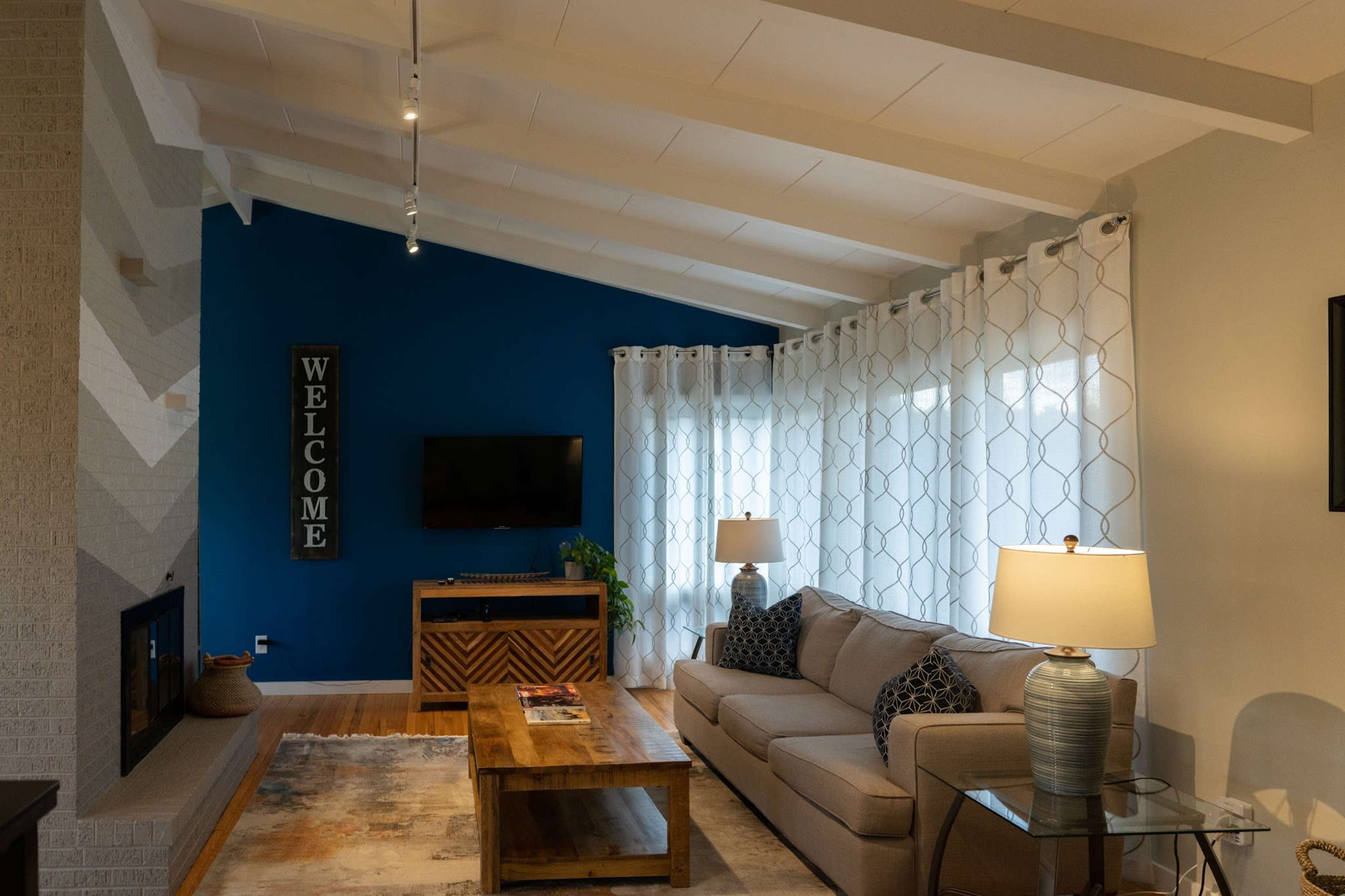 A modern living room features a gray sofa, wooden coffee table, and a blue accent wall with a mounted TV.