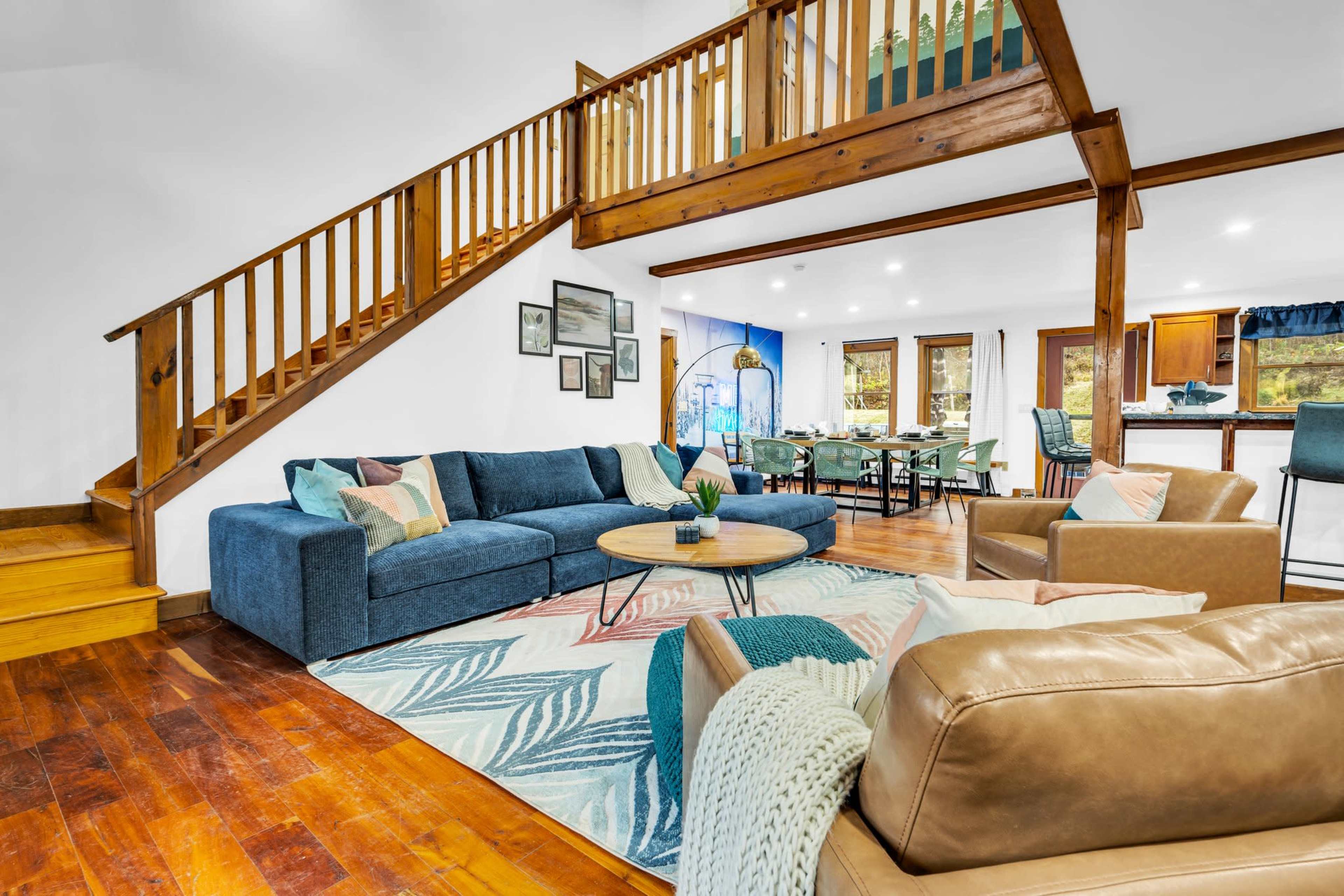 A spacious living area with a blue sofa, a round coffee table, and a staircase leading to an upper level, adjacent to a dining area and kitchen.