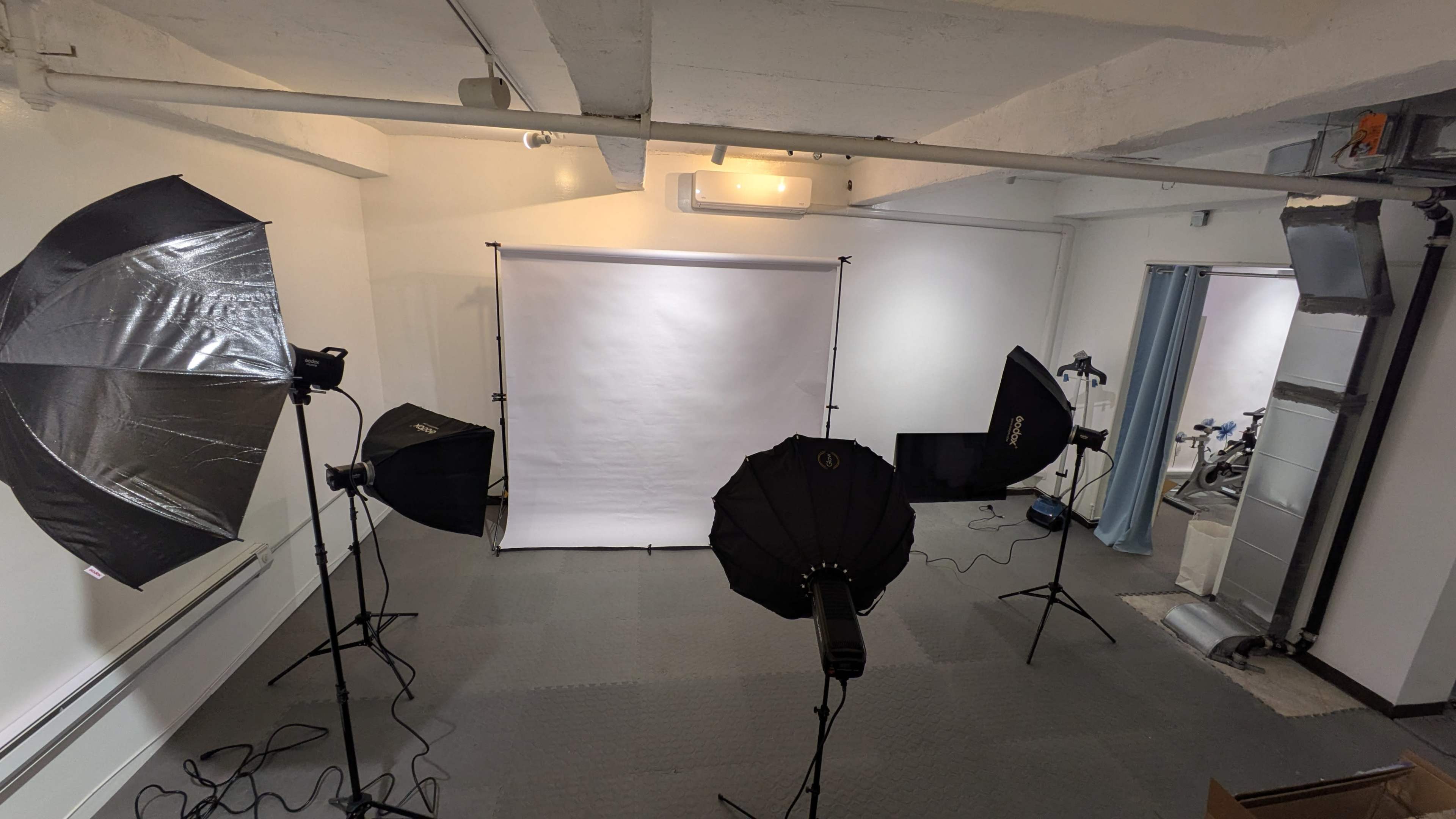 The image shows a photography studio setup with multiple light stands, softboxes, and a blank backdrop in an indoor space.