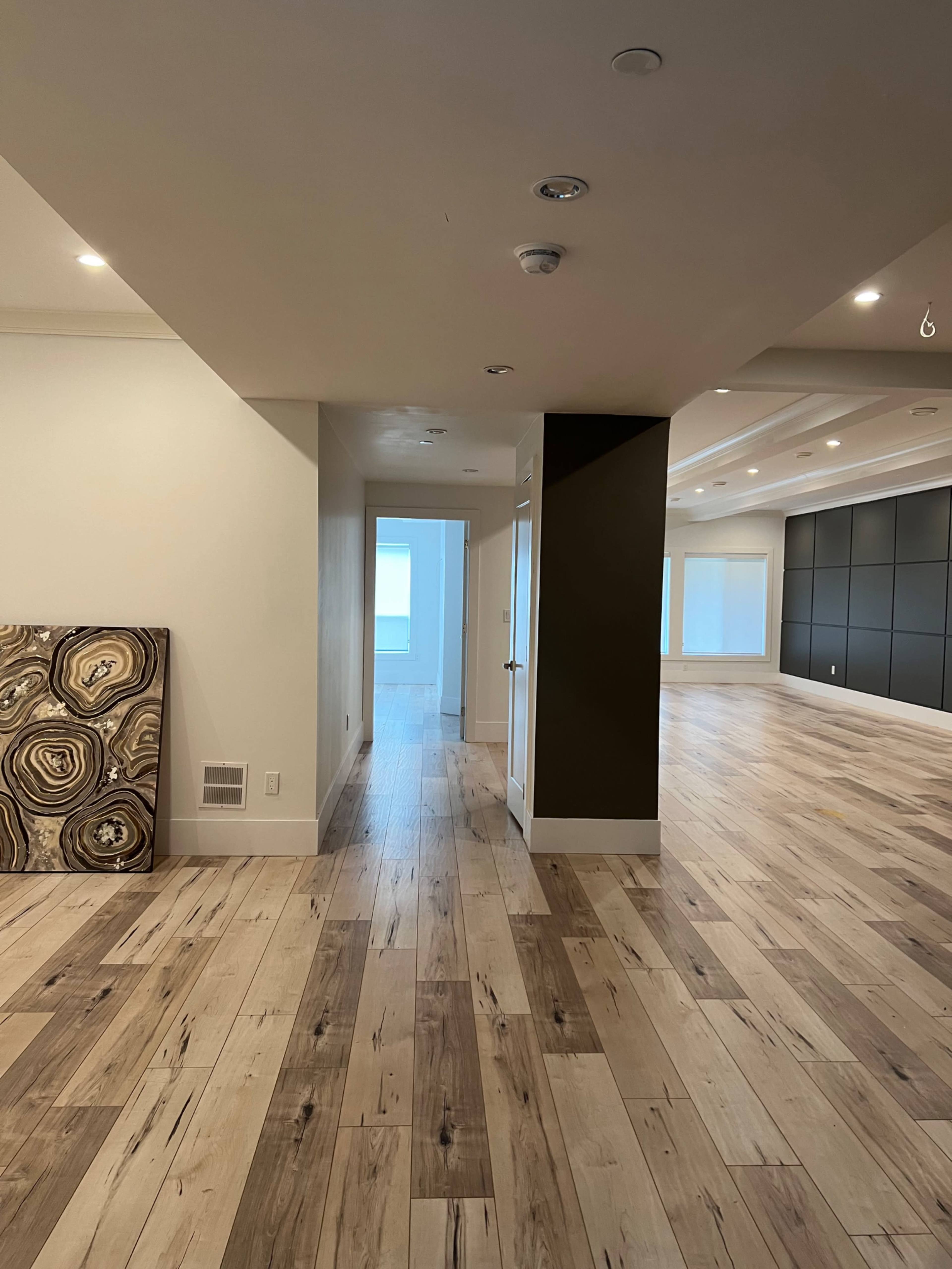 A spacious interior with wooden flooring, featuring a hallway leading to an open area with large windows.