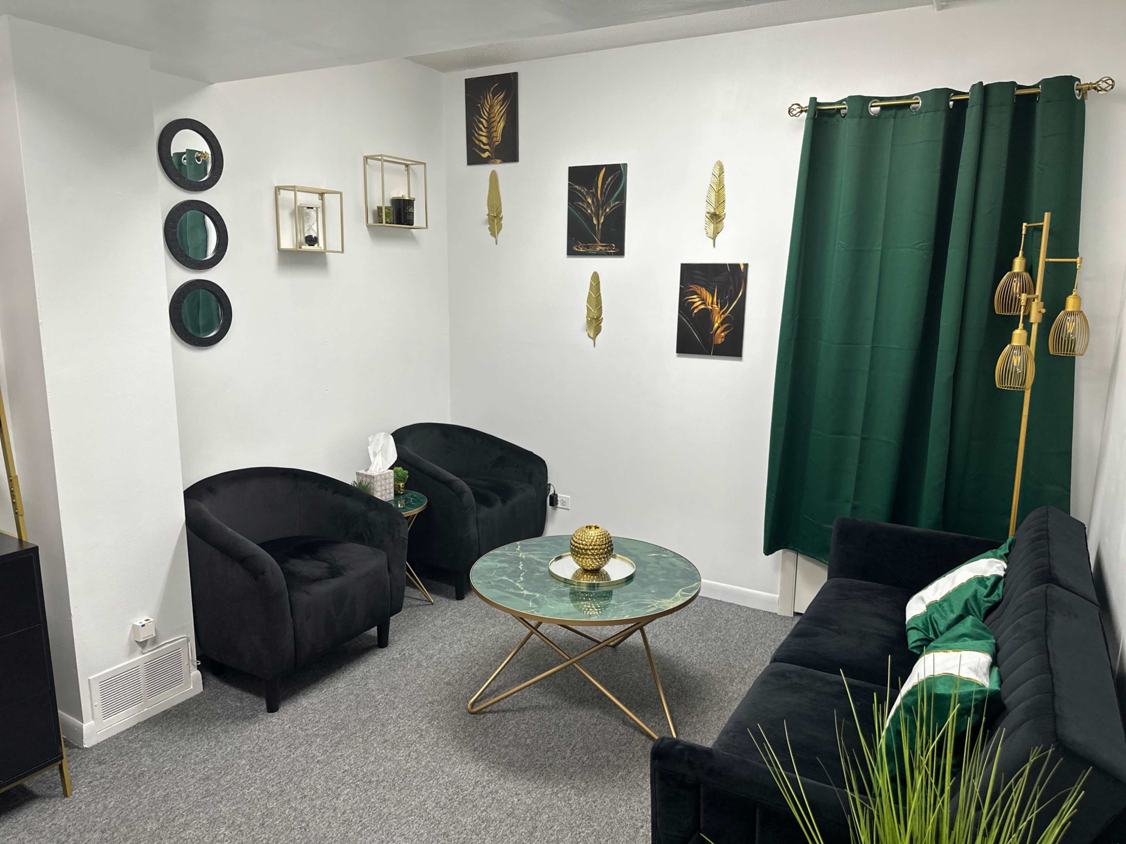 A modern living room with black furniture, a green curtain, gold accents, and wall art featuring plant themes.