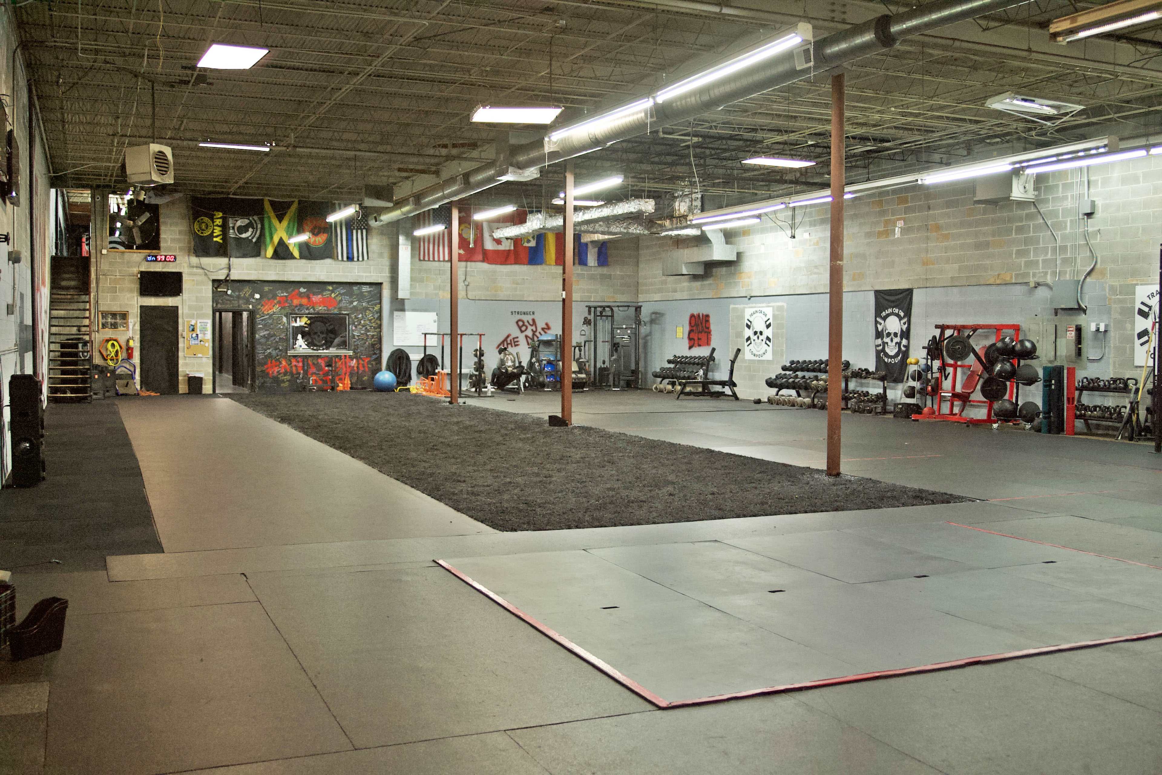 The image shows a spacious gym interior with workout equipment, a turf area for exercises, and a minimalist design featuring painted walls and various flags.