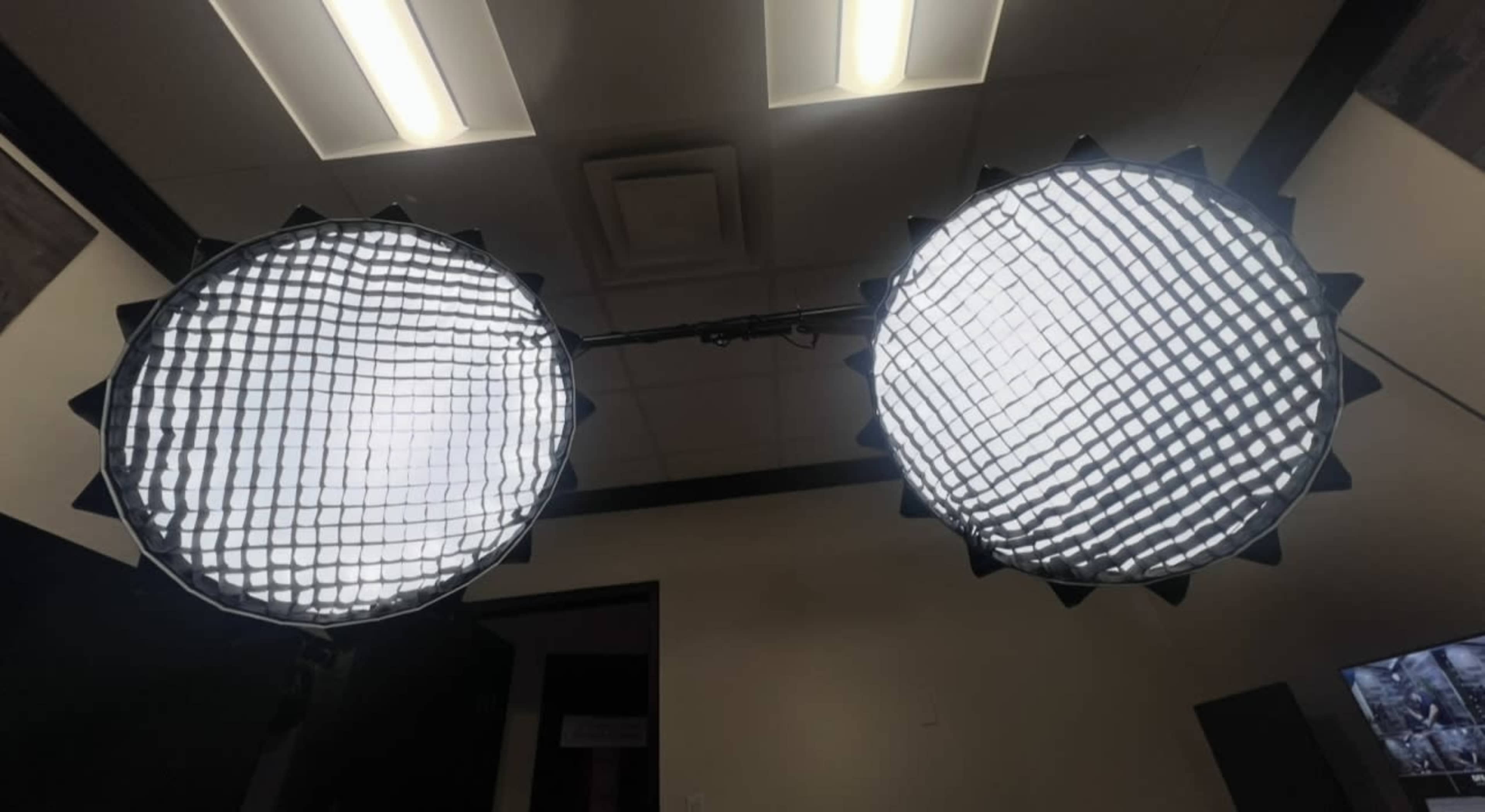 The image shows two large softbox lights mounted on a stand in a room with a ceiling and wall.