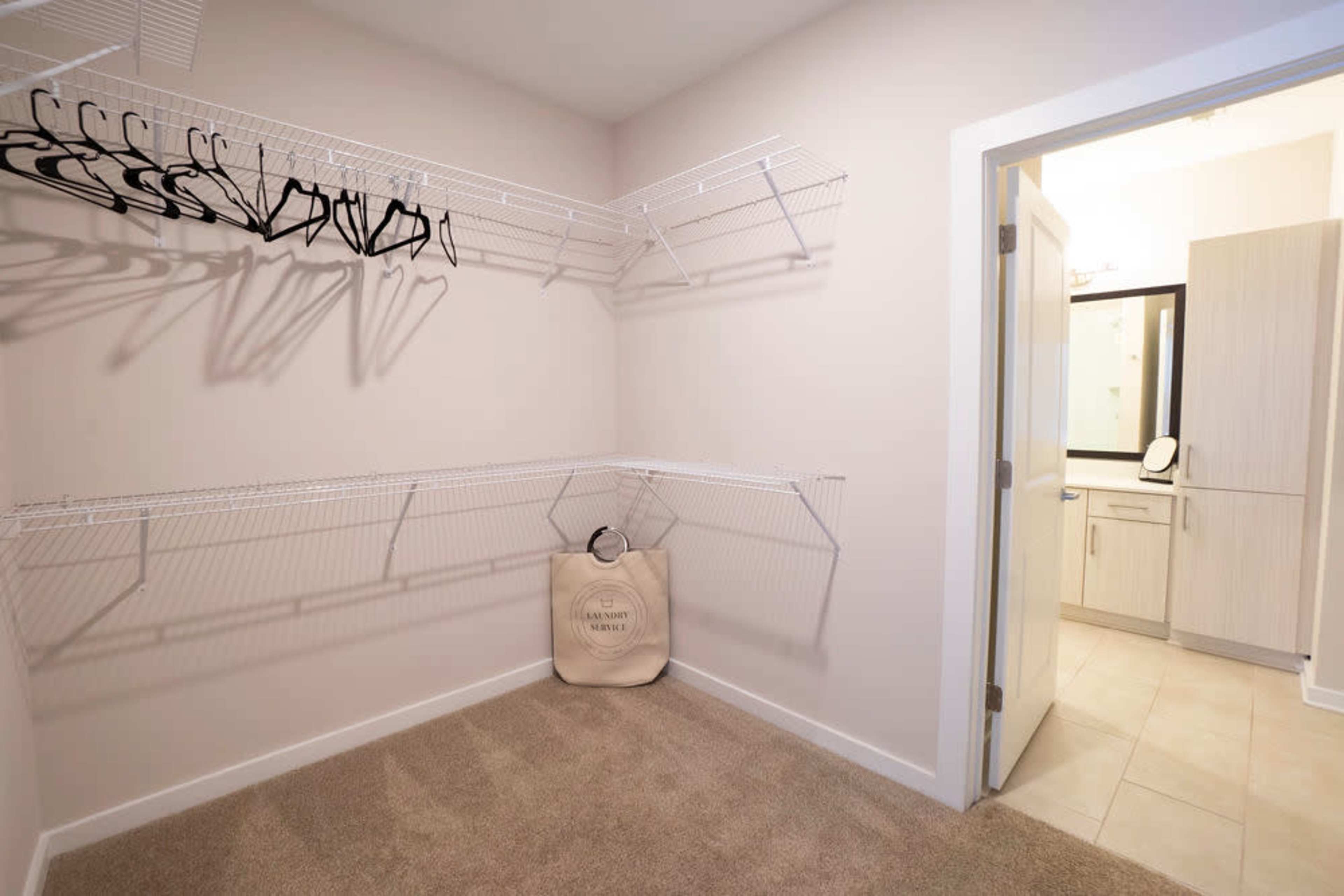 A lightly furnished closet with wire shelving on two walls and a laundry basket placed on the carpeted floor.