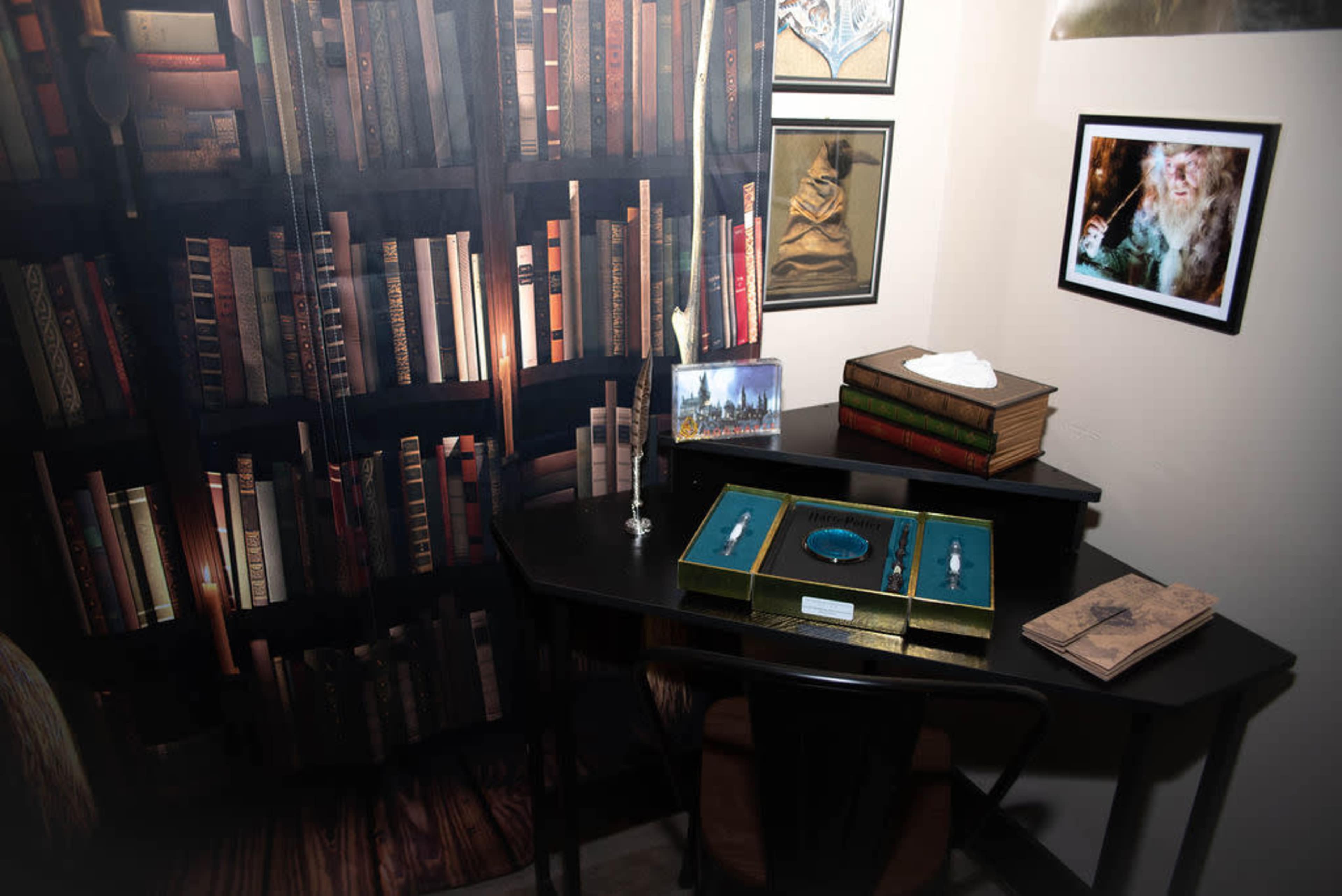 A small desk with a display of jewelry boxes and books, set against a backdrop of a bookshelf filled with various books and a few framed pictures on the wall.
