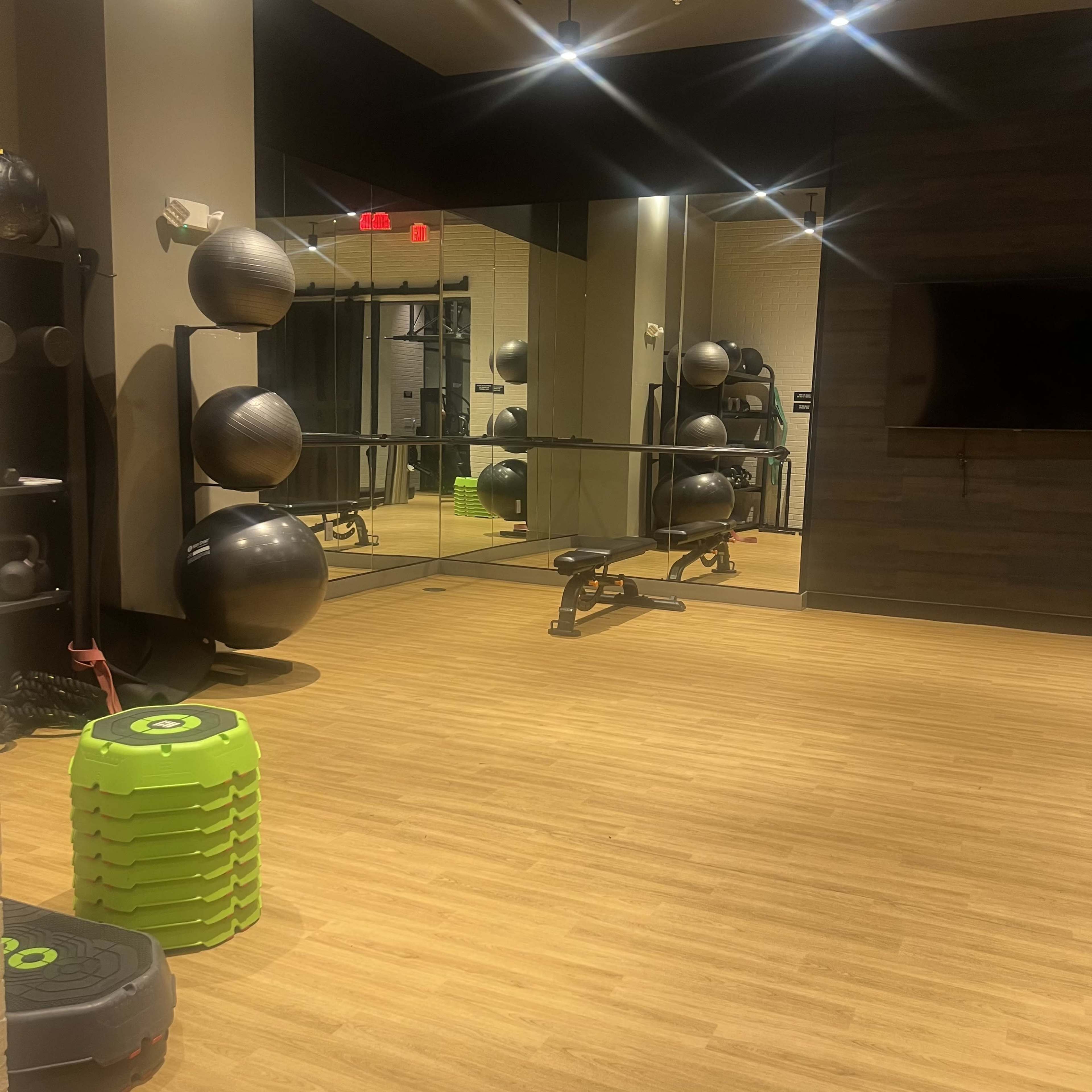 The image shows a fitness studio featuring exercise equipment, a large mirror, and a wooden floor.