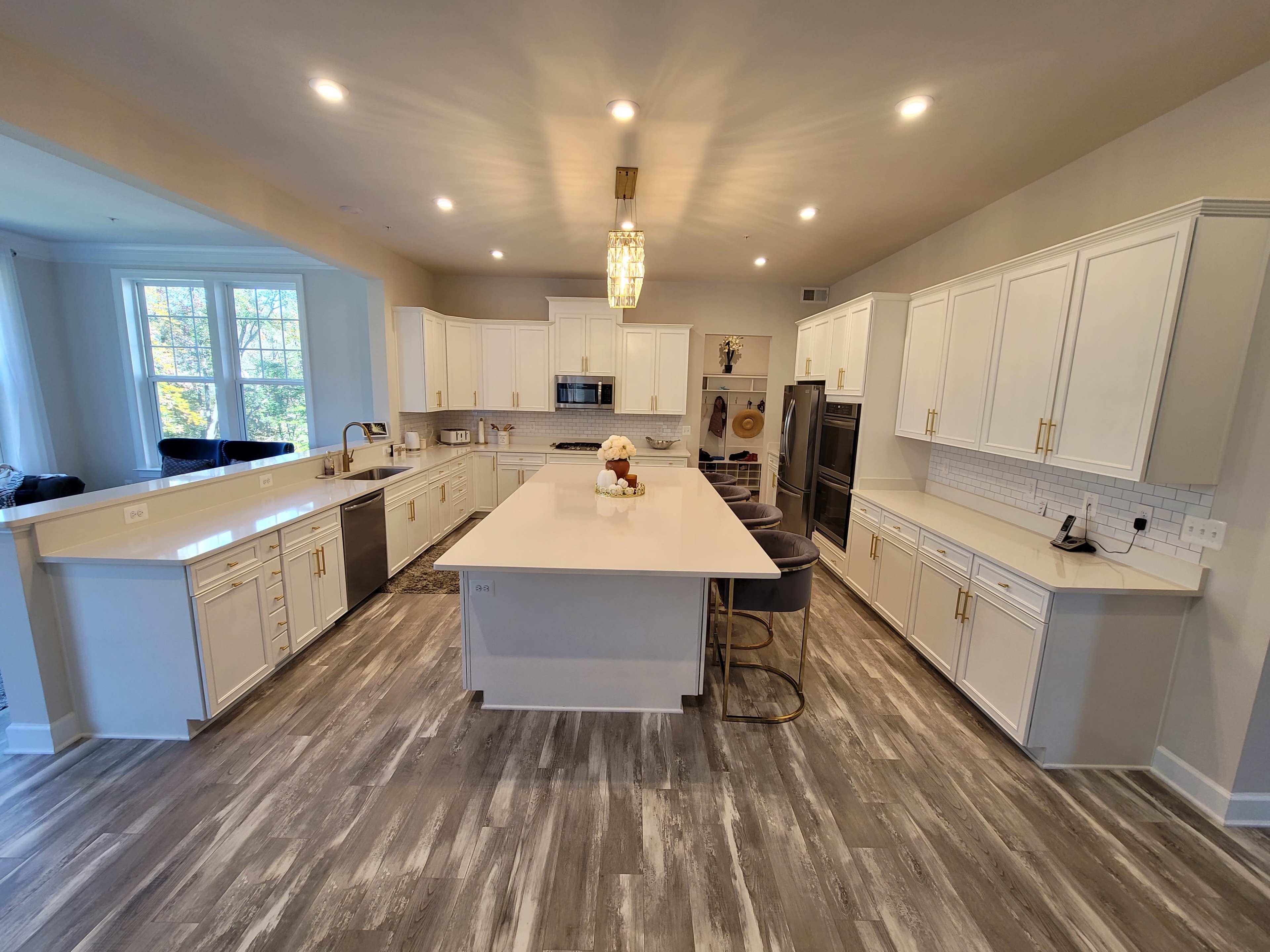 The image shows a modern kitchen with white cabinetry, a large island, and stainless steel appliances, illuminated by pendant lights.