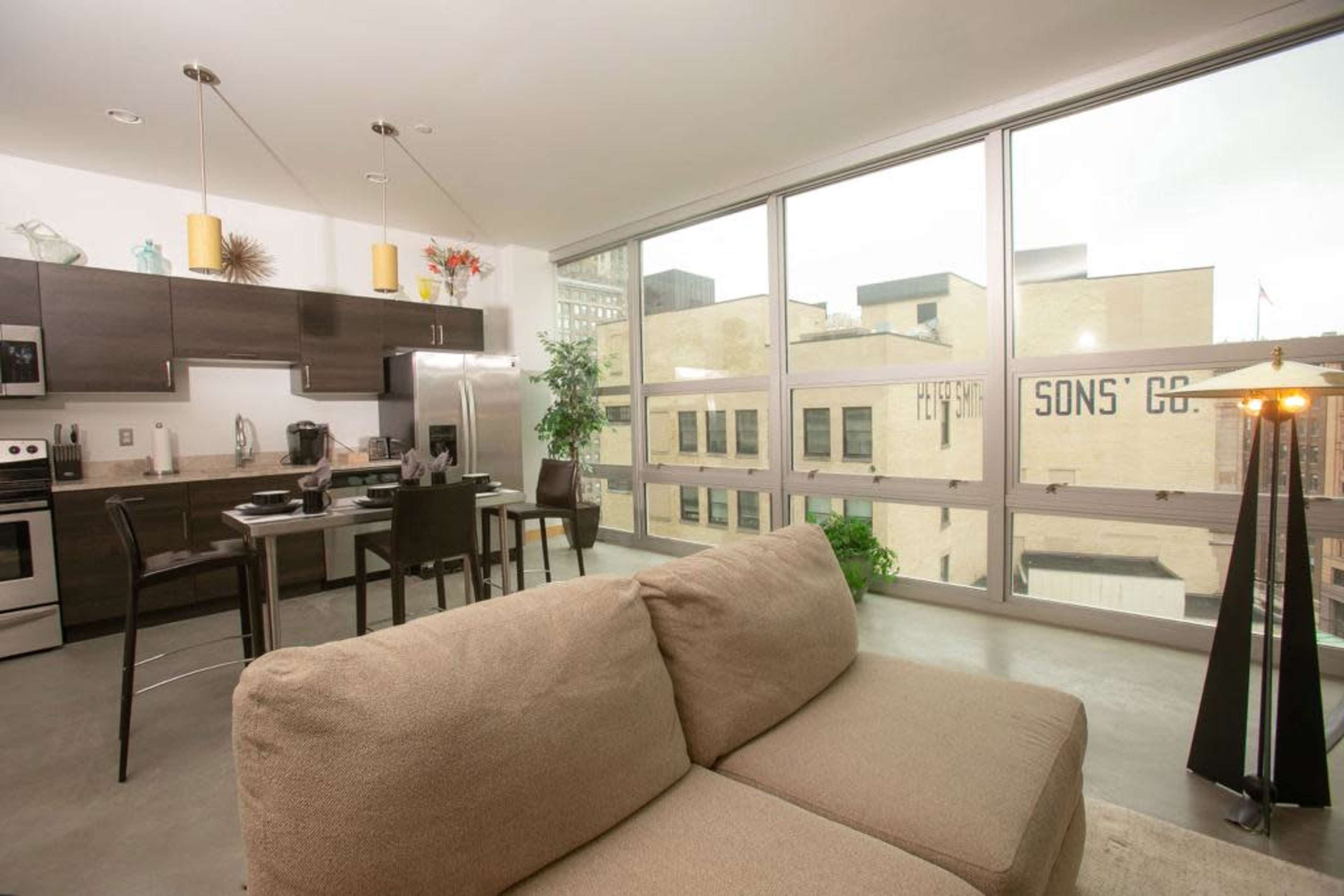 A modern apartment with a living area featuring a sofa, a dining area with a table and chairs, and large windows that overlook a cityscape.