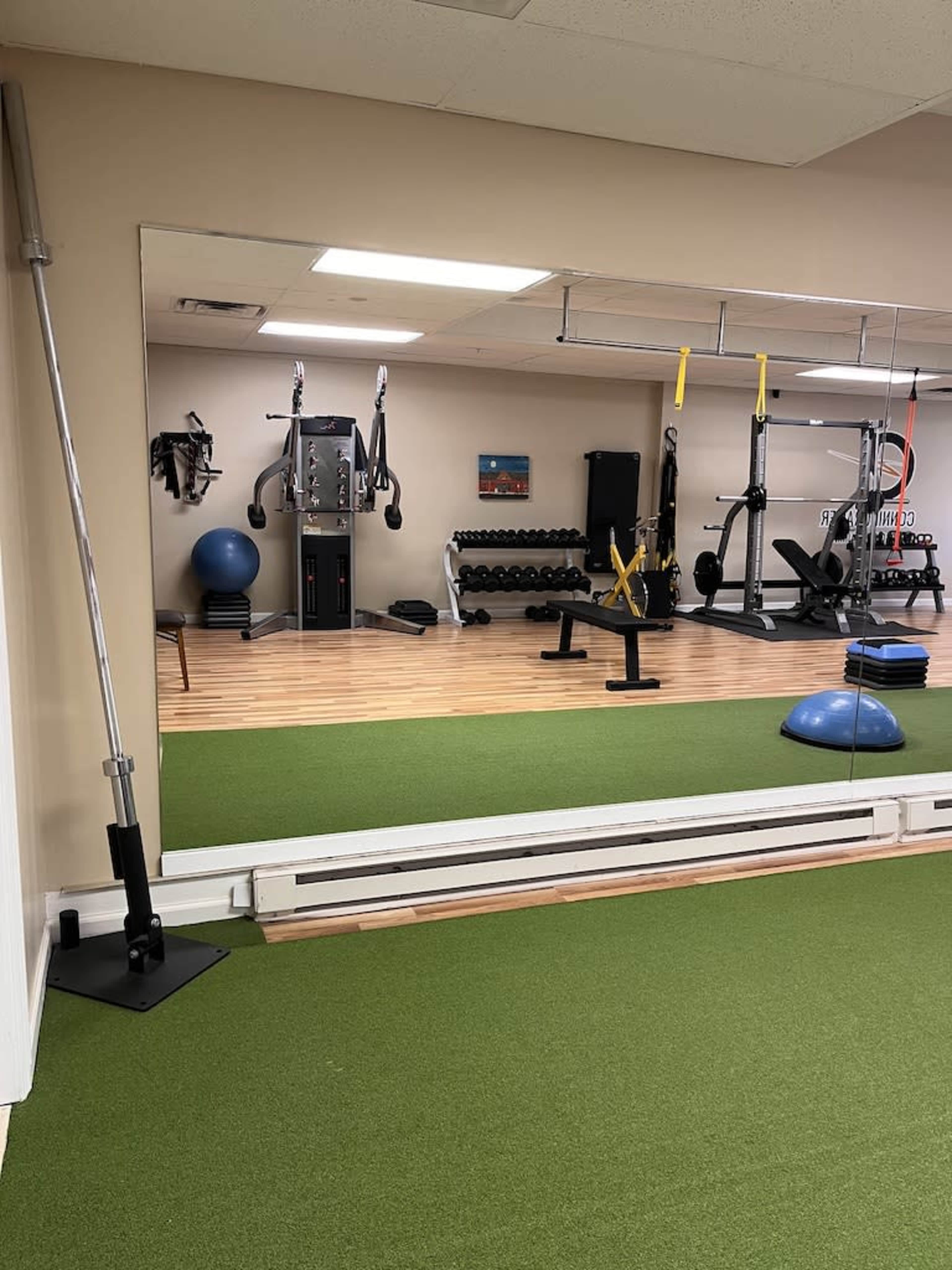 A fitness studio with exercise equipment, including weights, resistance machines, and yoga accessories, reflected in a large mirror.