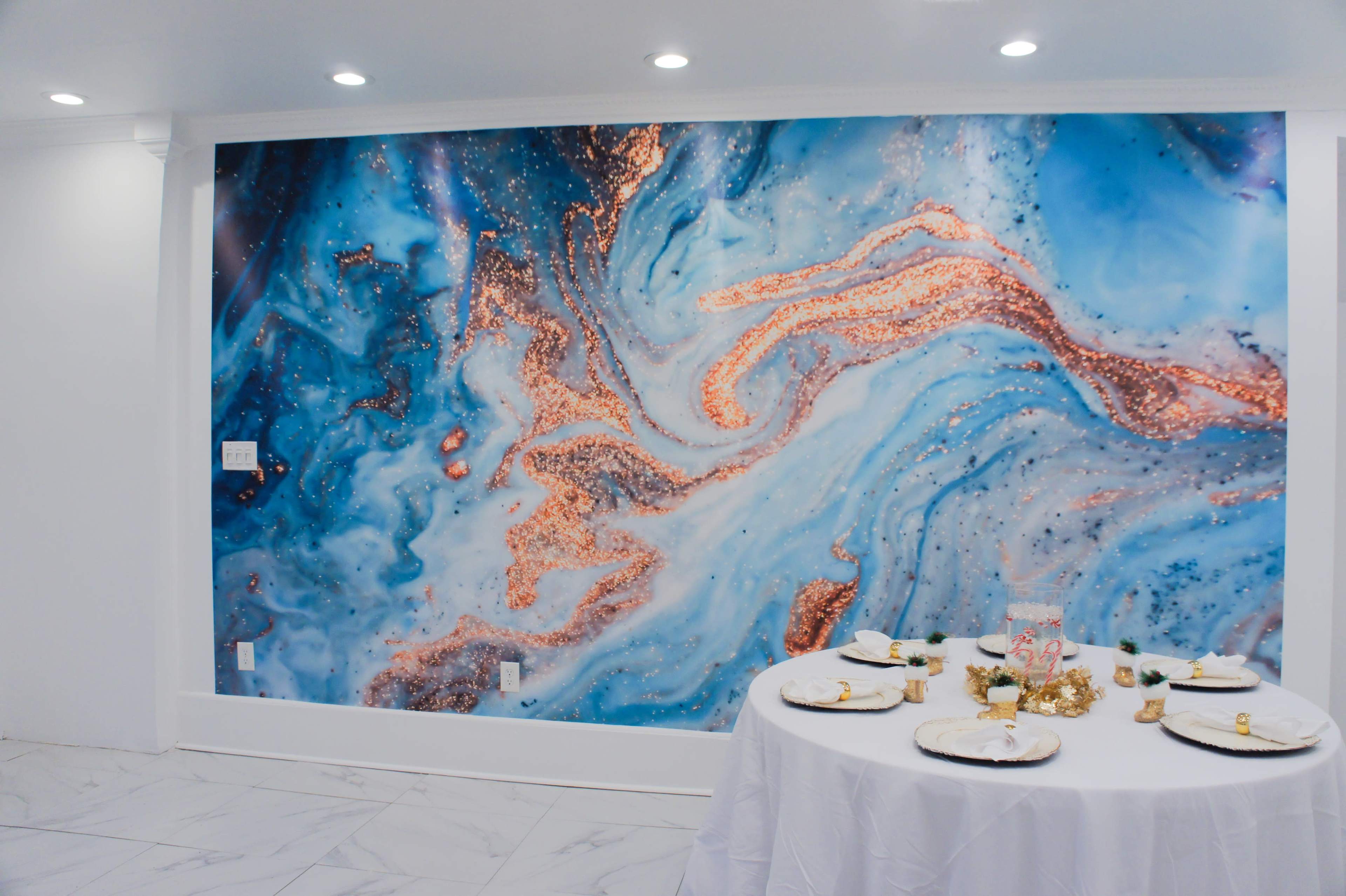 A round table is set with plates and decorations in front of a large blue and gold abstract wall mural.