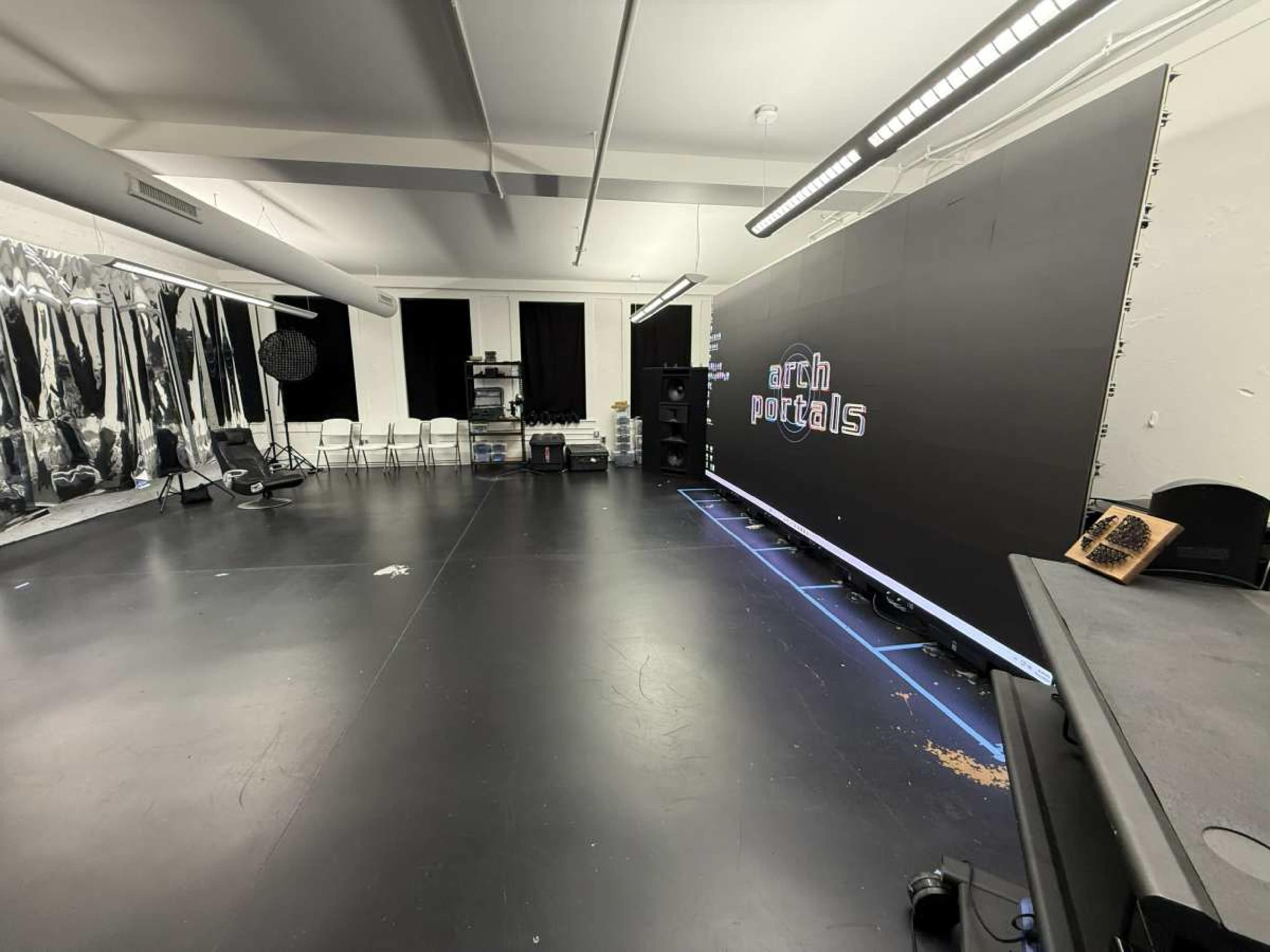 The image shows an empty studio space with a large black backdrop displaying the text "arch portals," surrounded by chairs and various equipment.