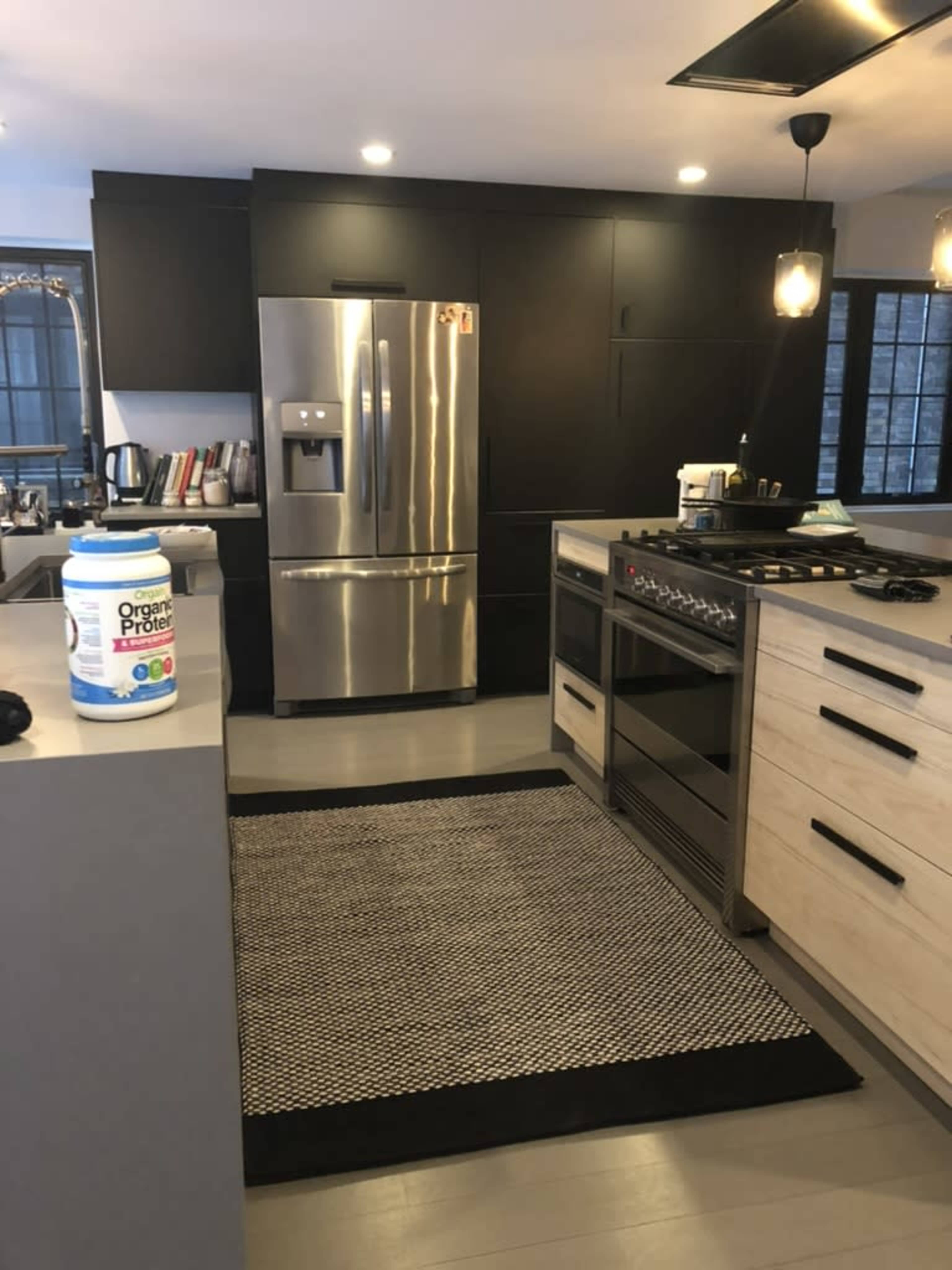 A modern kitchen featuring a stainless steel refrigerator, a gas stove, and a central island with a black and white rug.