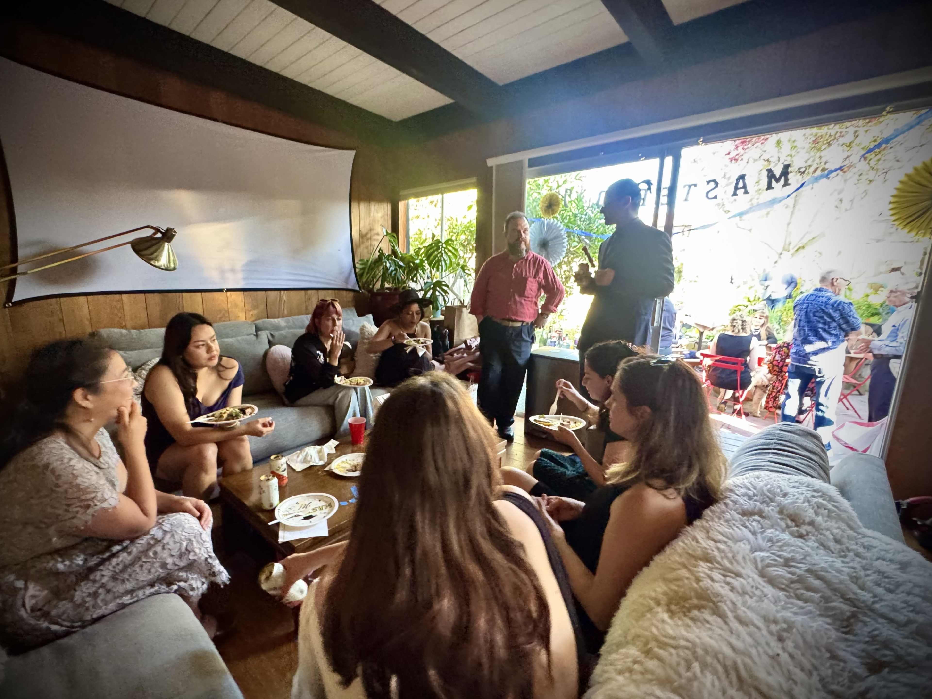 A group of people is gathered in a cozy living room, enjoying food and conversation.