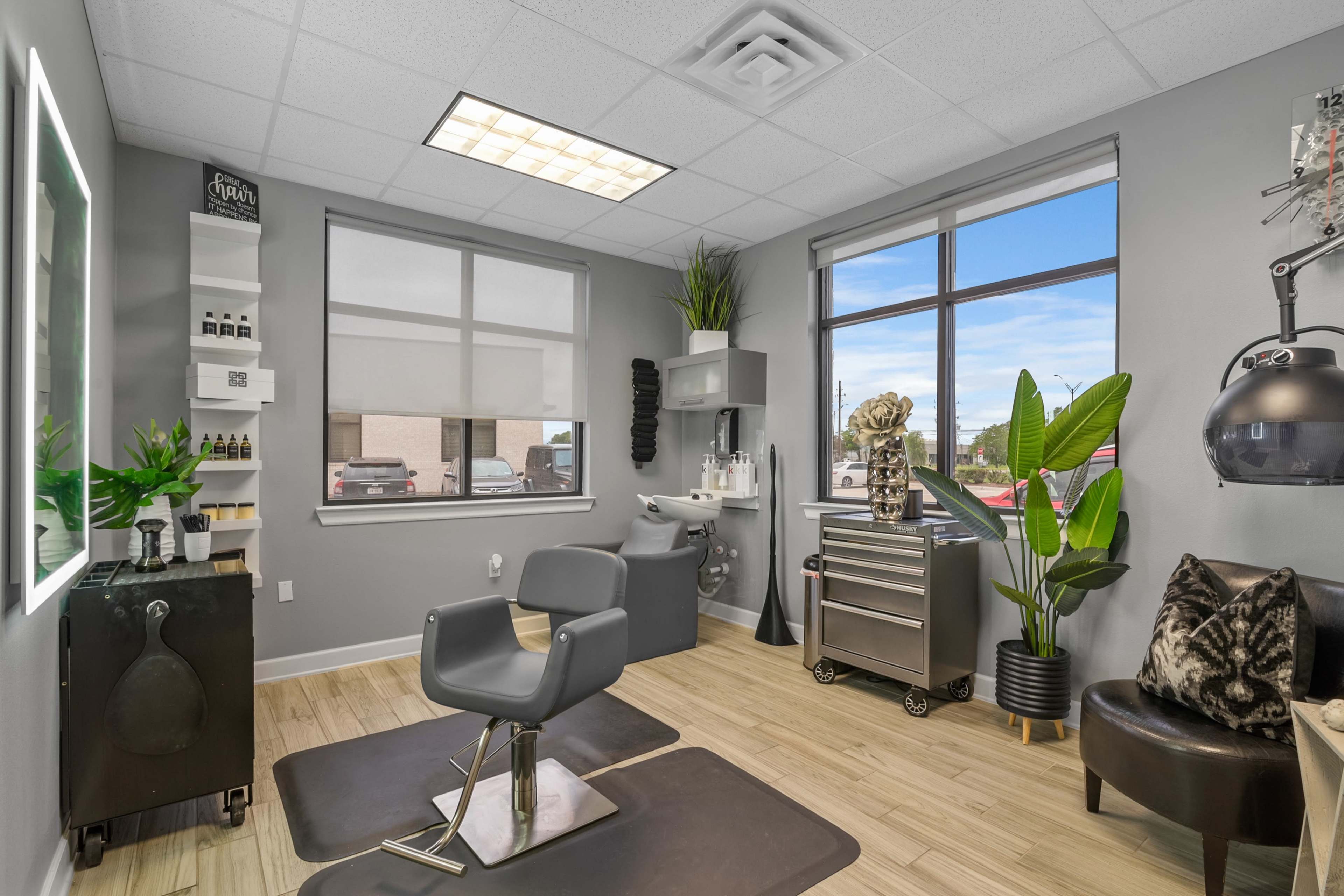 A modern salon interior featuring a styling chair, a storage cart, and large windows with daylight.