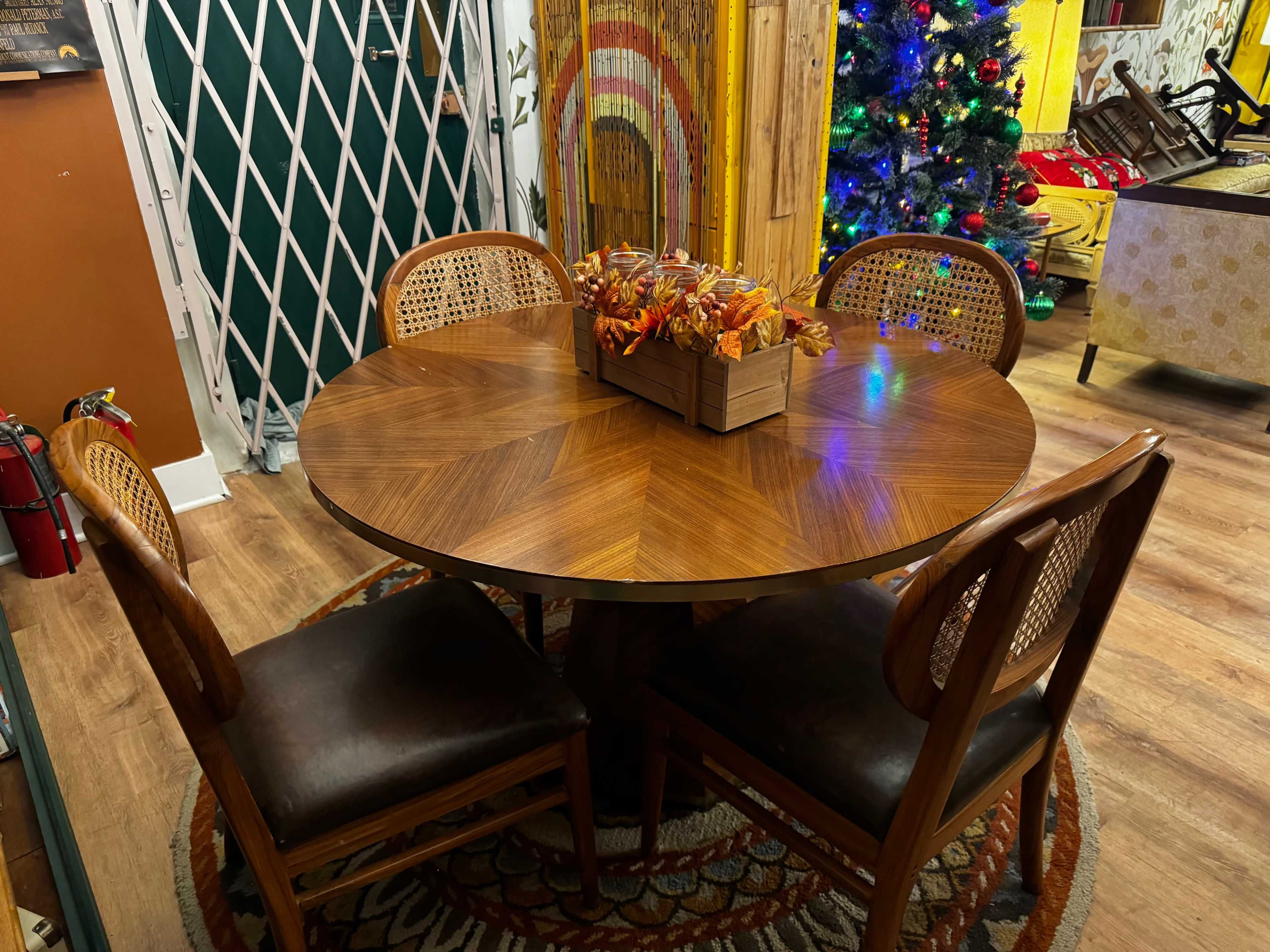 A round wooden dining table with a decorative centerpiece of autumn leaves is surrounded by four chairs in a warmly lit room.