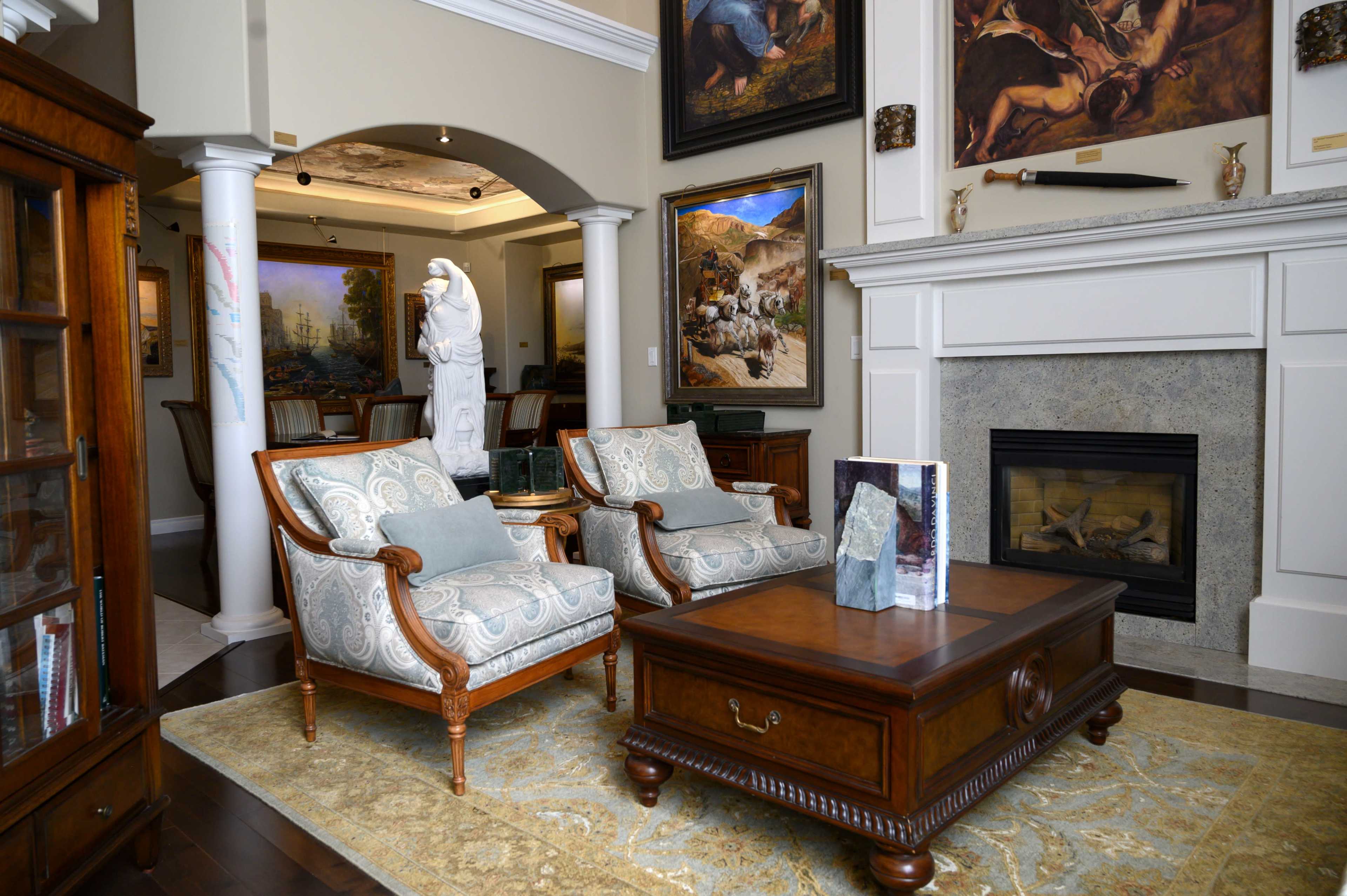 The image shows a well-furnished living room with two upholstered chairs, a wooden coffee table, and a fireplace surrounded by decorative art and sculptures.