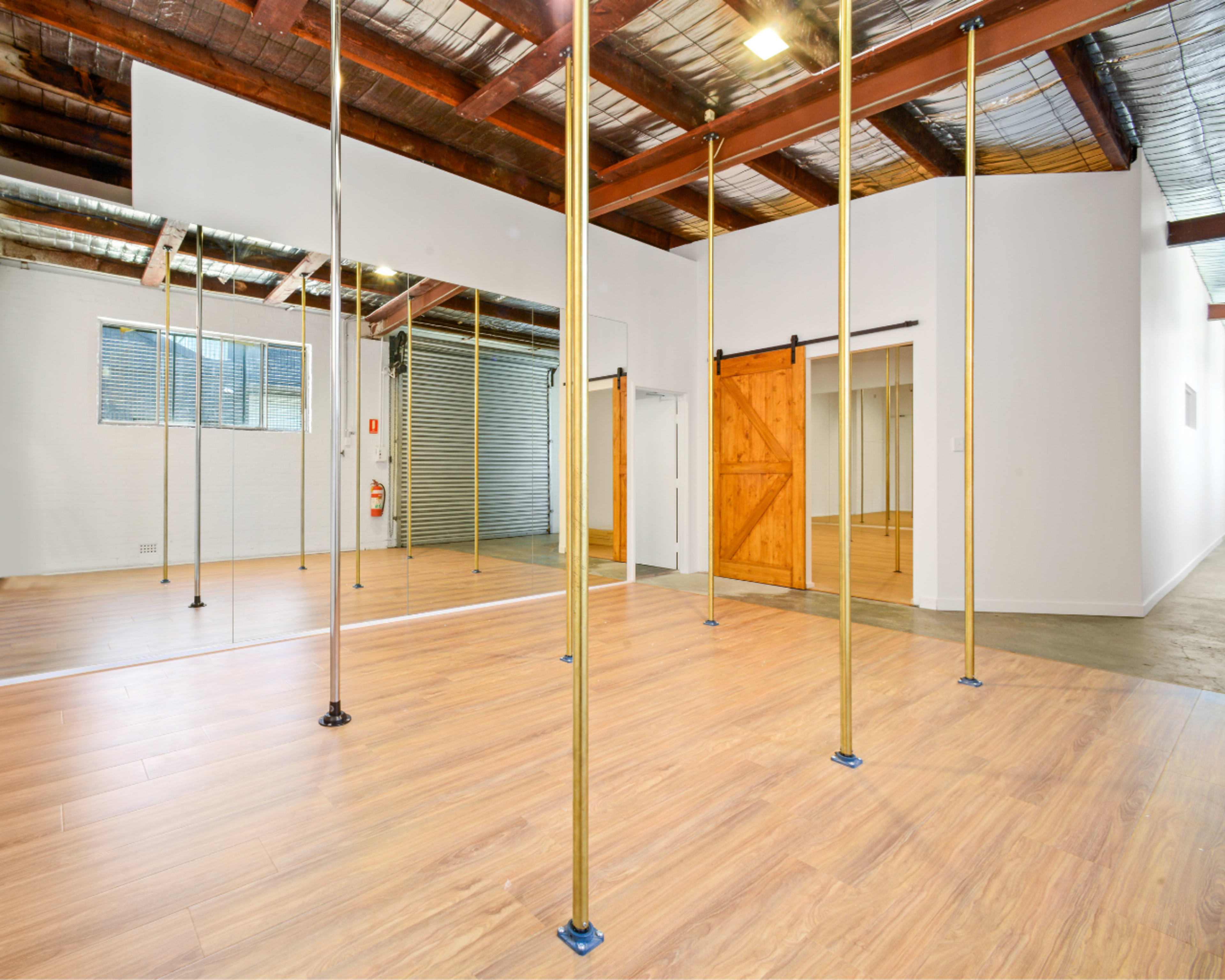 The image shows an open studio space with wooden floors, gold poles, mirrors, and sliding barn doors.