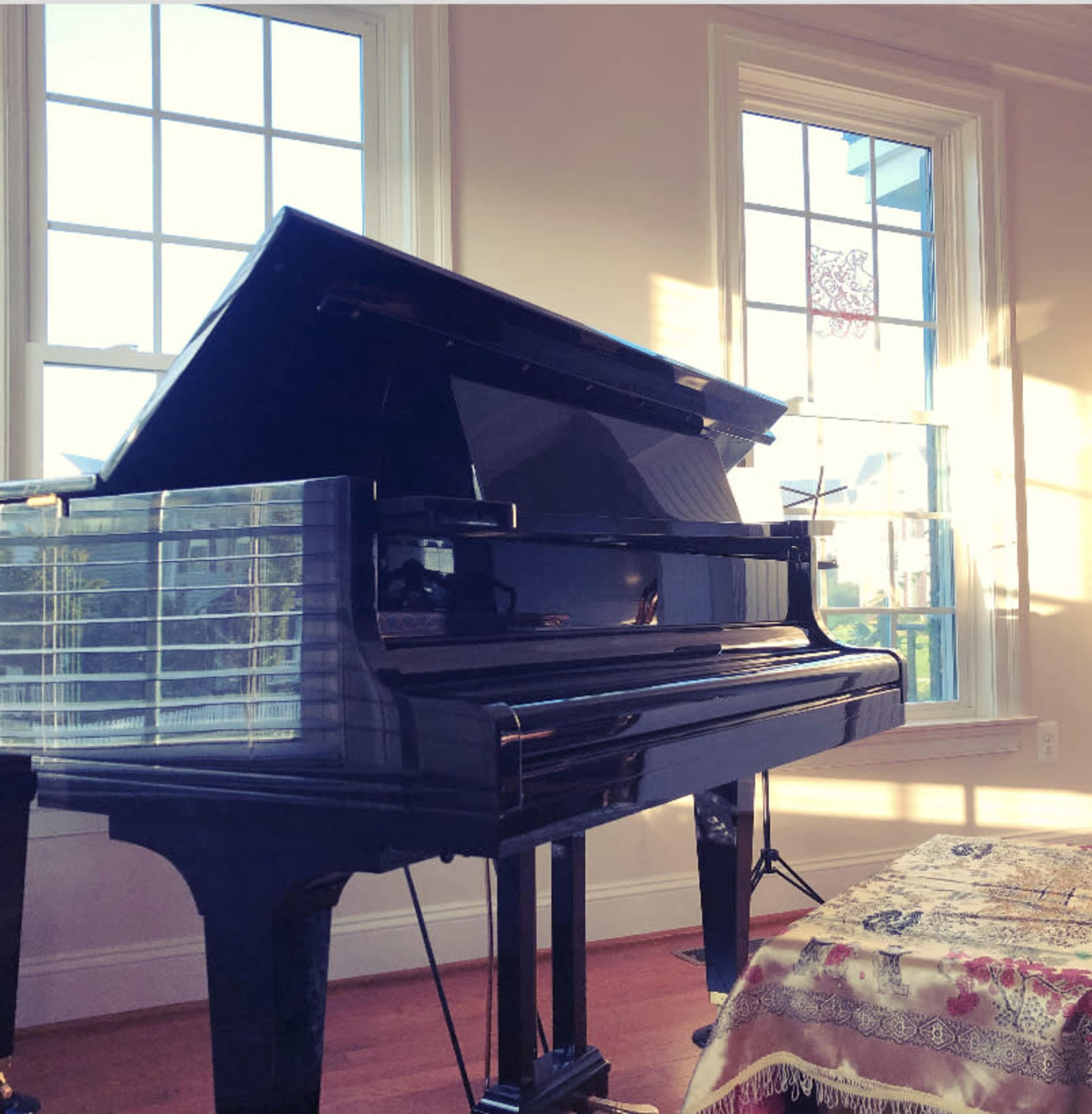 A grand piano is positioned near a window, with sunlight illuminating its glossy surface.
