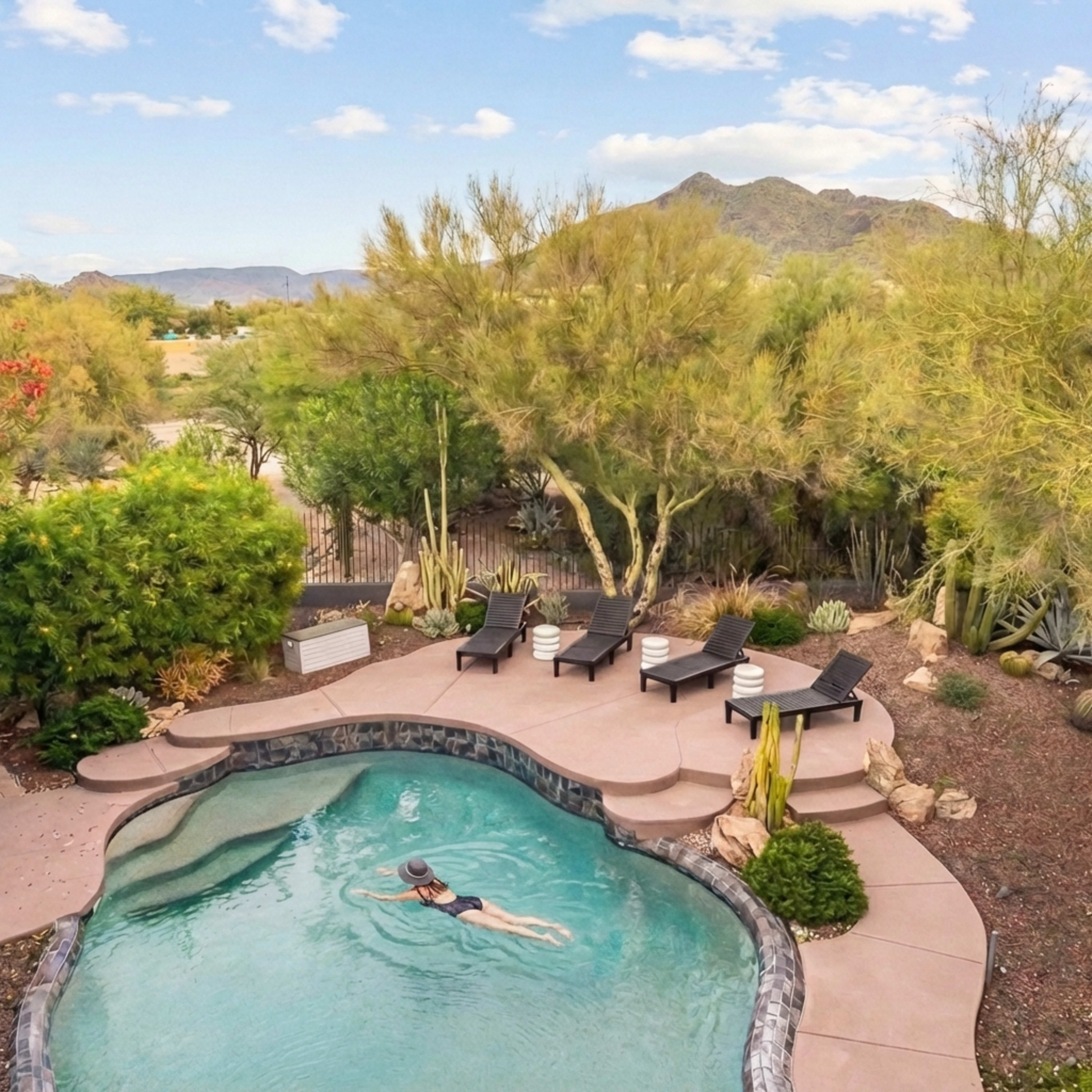 A person swims in a pool surrounded by desert landscaping and sun loungers under a clear sky.