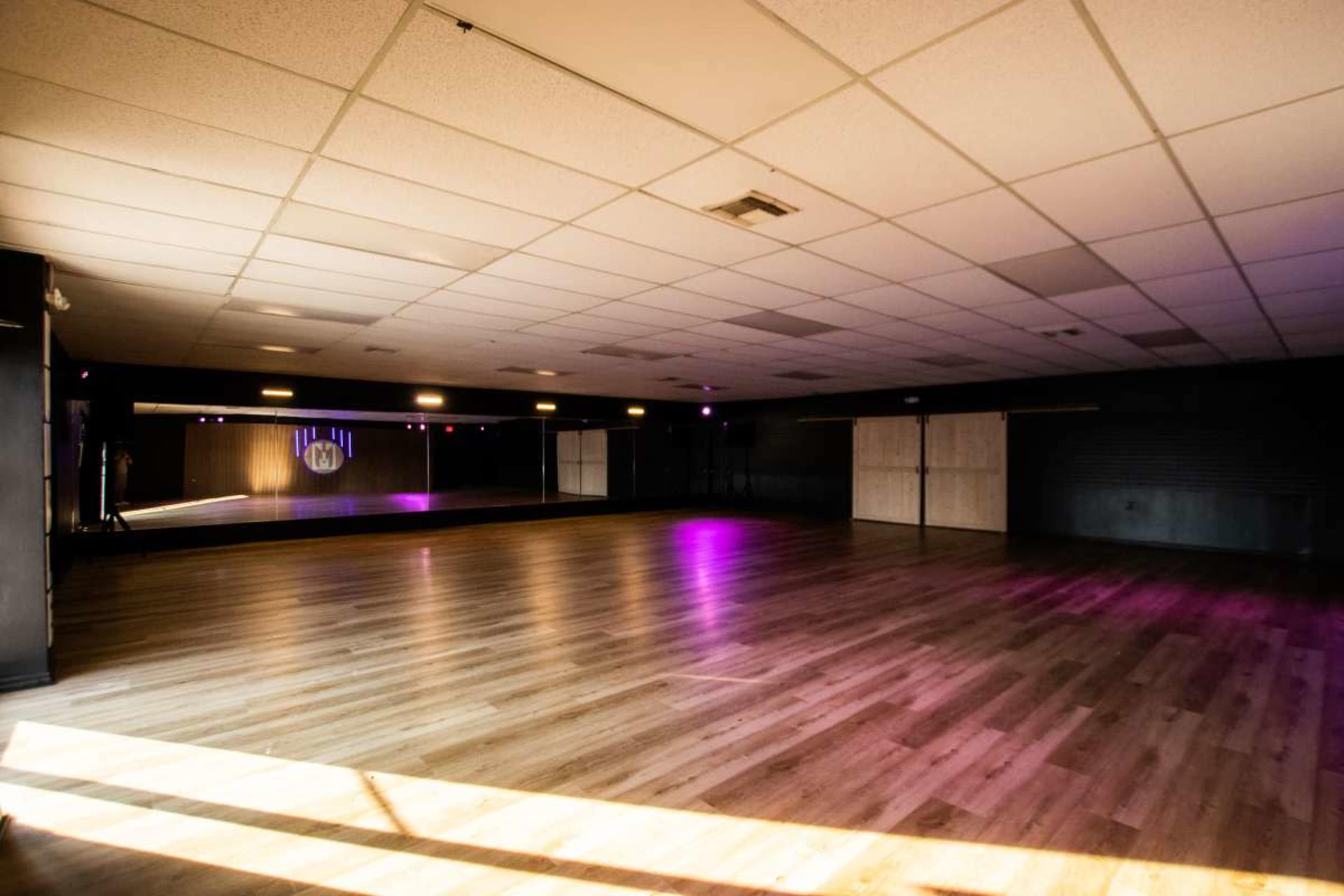 The image shows a spacious dance studio with wooden flooring and soft lighting.