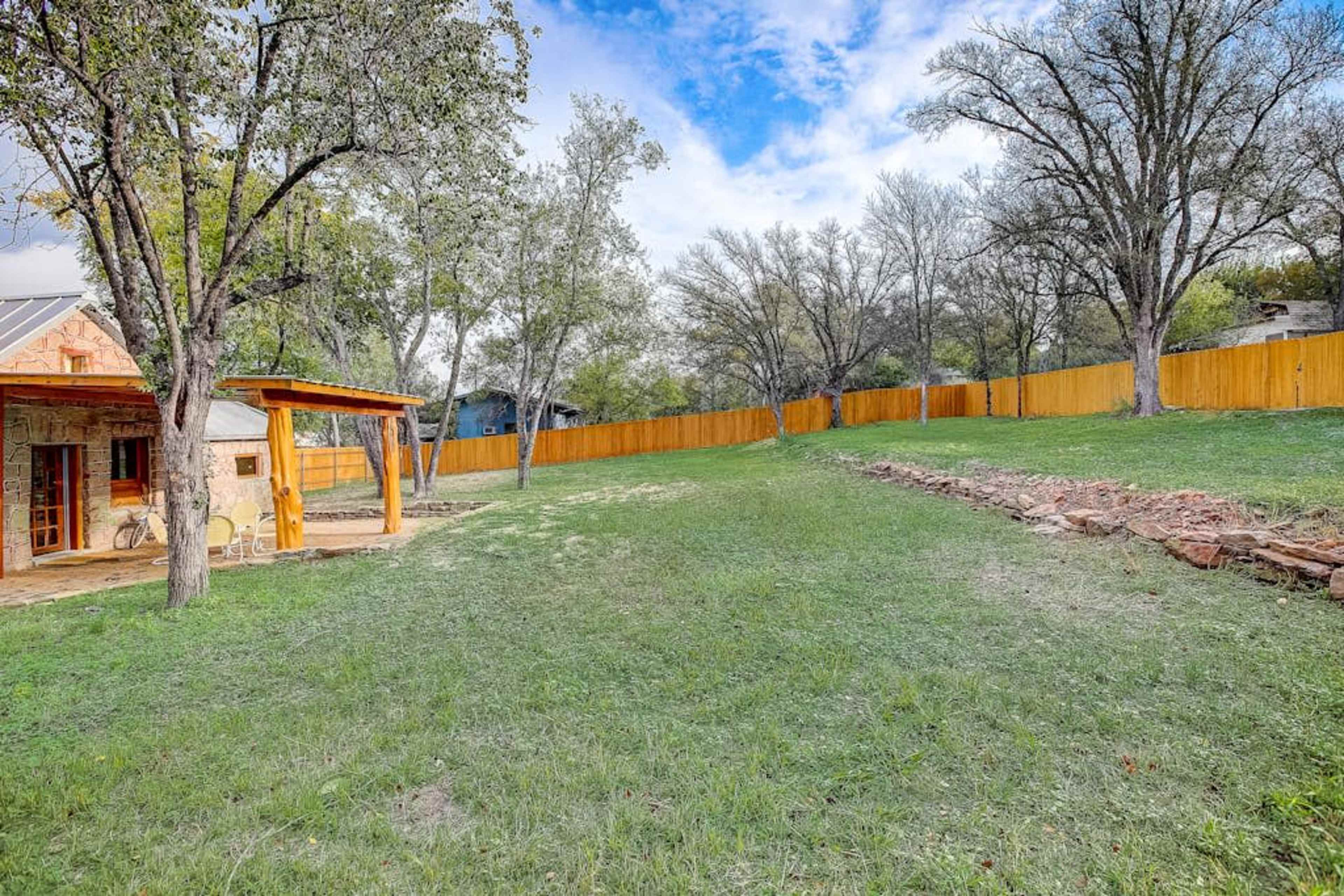 A grassy backyard with a fenced area, a small stone feature, and a covered patio attached to a house.