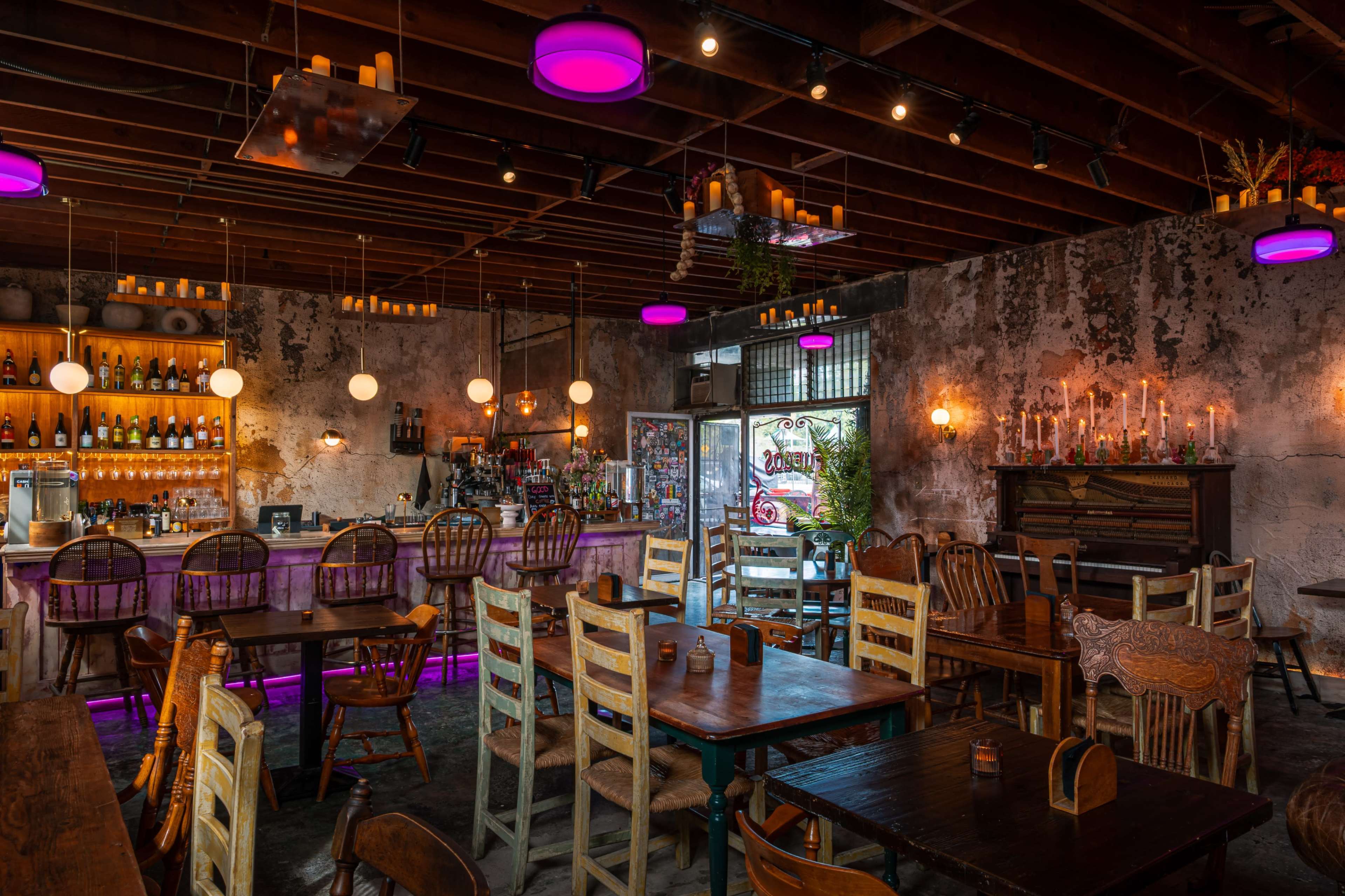 The image shows a rustic restaurant interior with wooden tables, chairs, and a bar illuminated by colorful pendant lights.