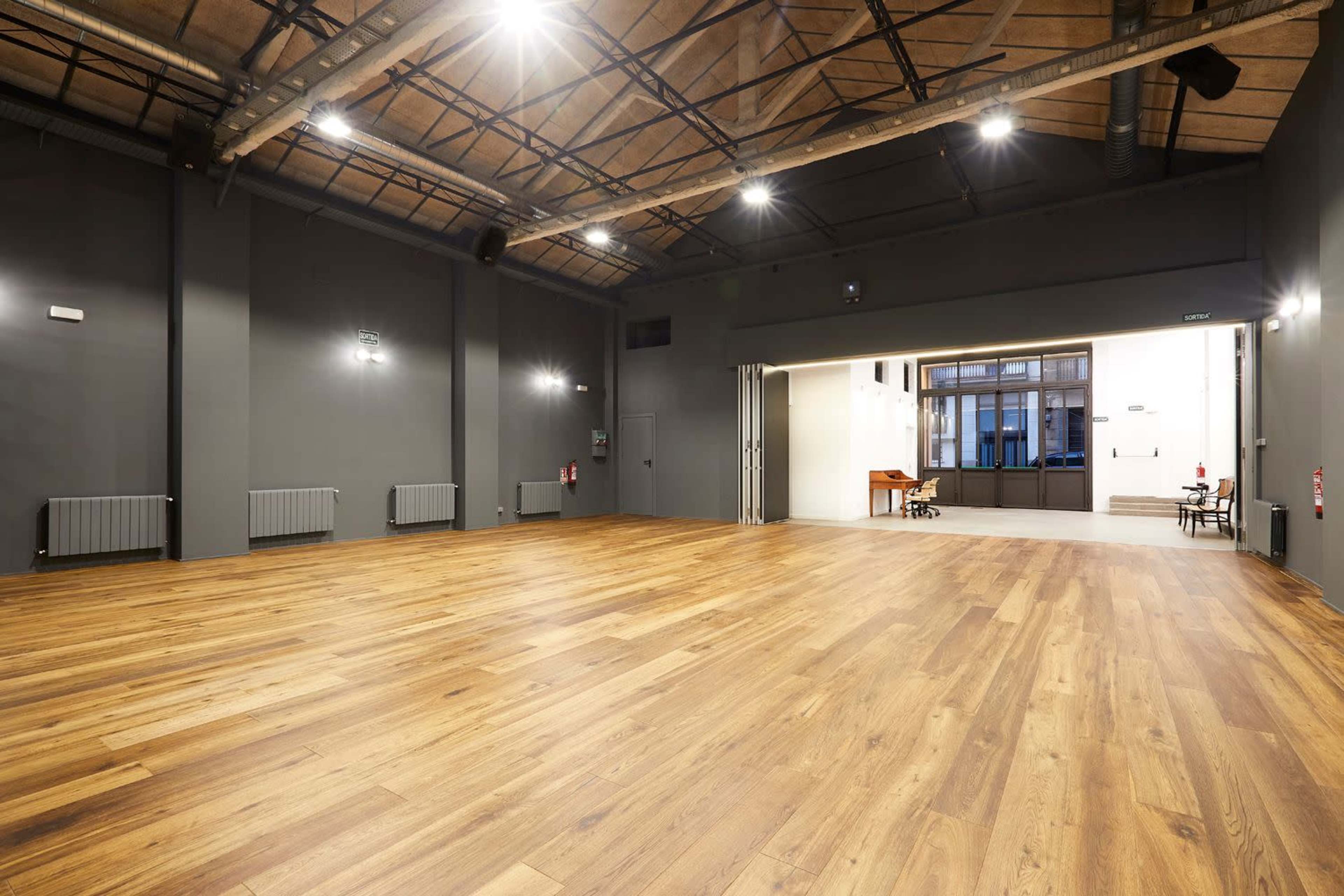 A spacious, empty hall with wooden flooring and high ceilings, featuring gray walls and soft lighting.