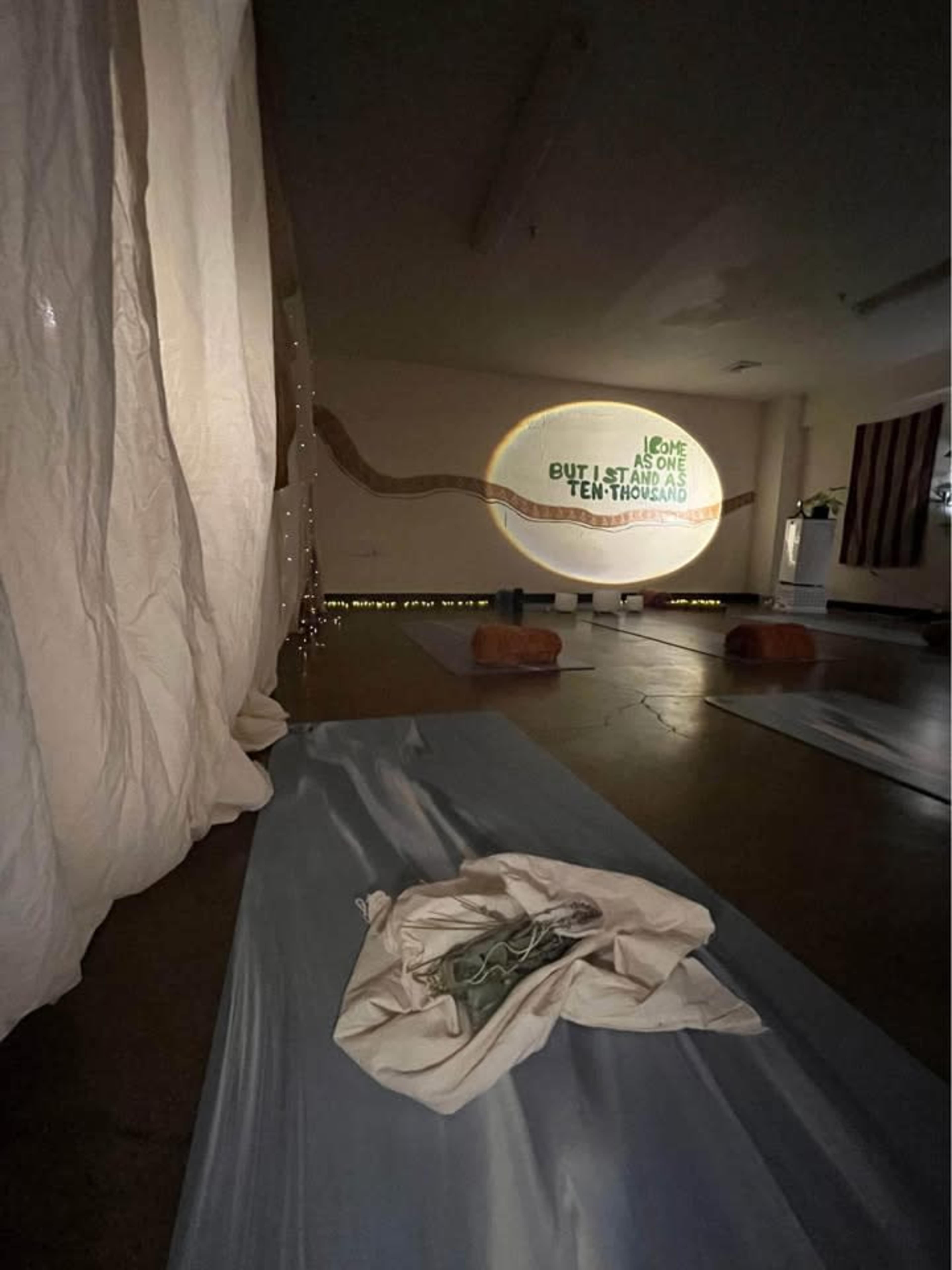 The image shows a meditation space with yoga mats on the floor and a projected message on the wall alongside soft white fabric draping.