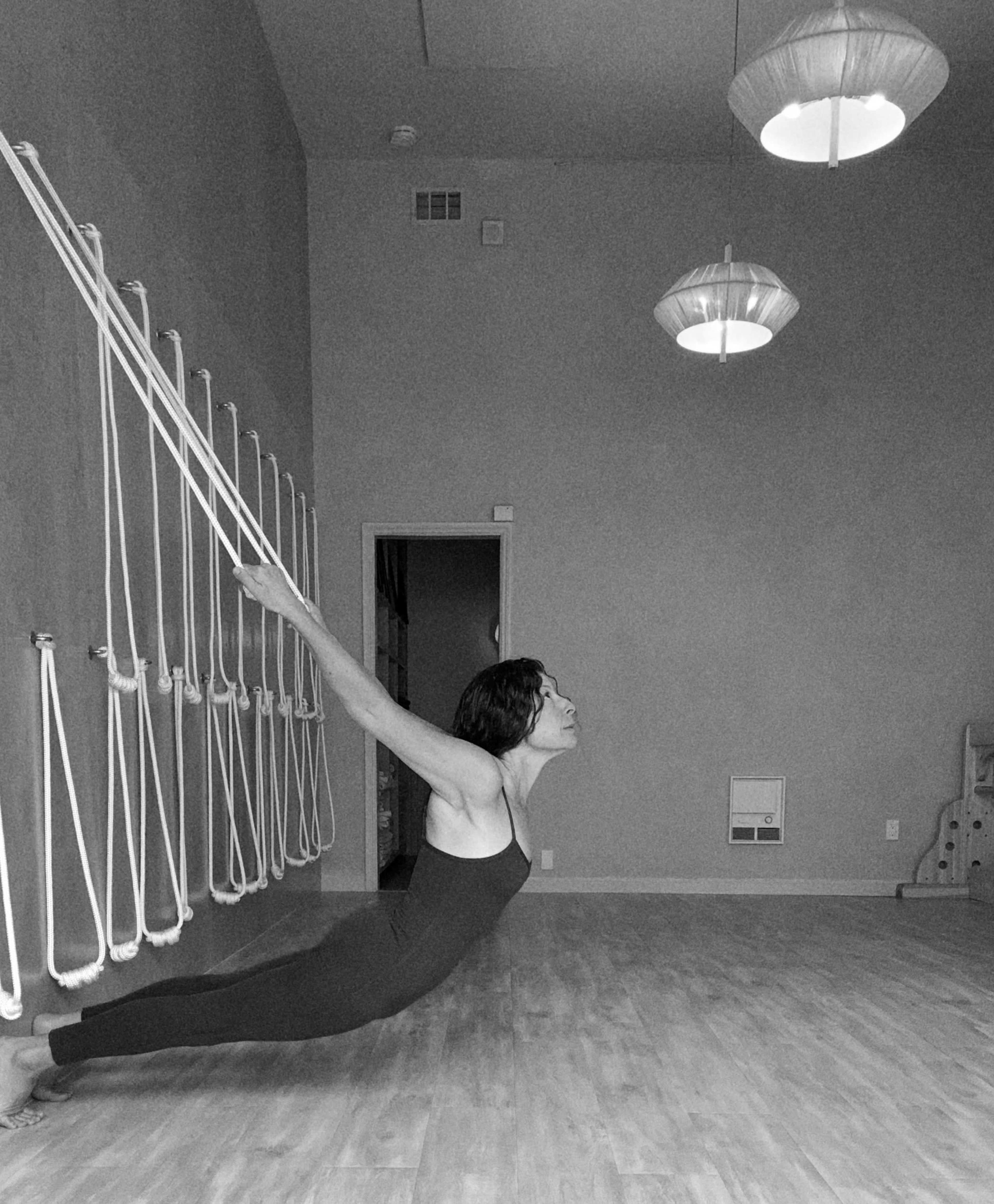A person performs a yoga pose using ropes attached to the wall in a minimalist studio.